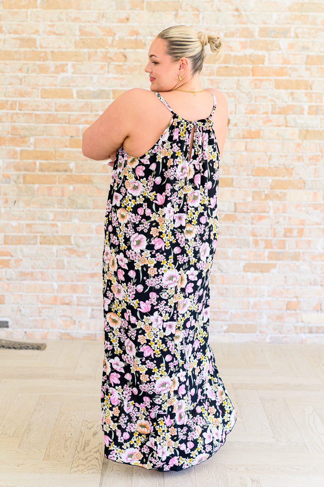 Plus size woman turning back wearing a black dress with pink and yellow floral print and thin straps indoors