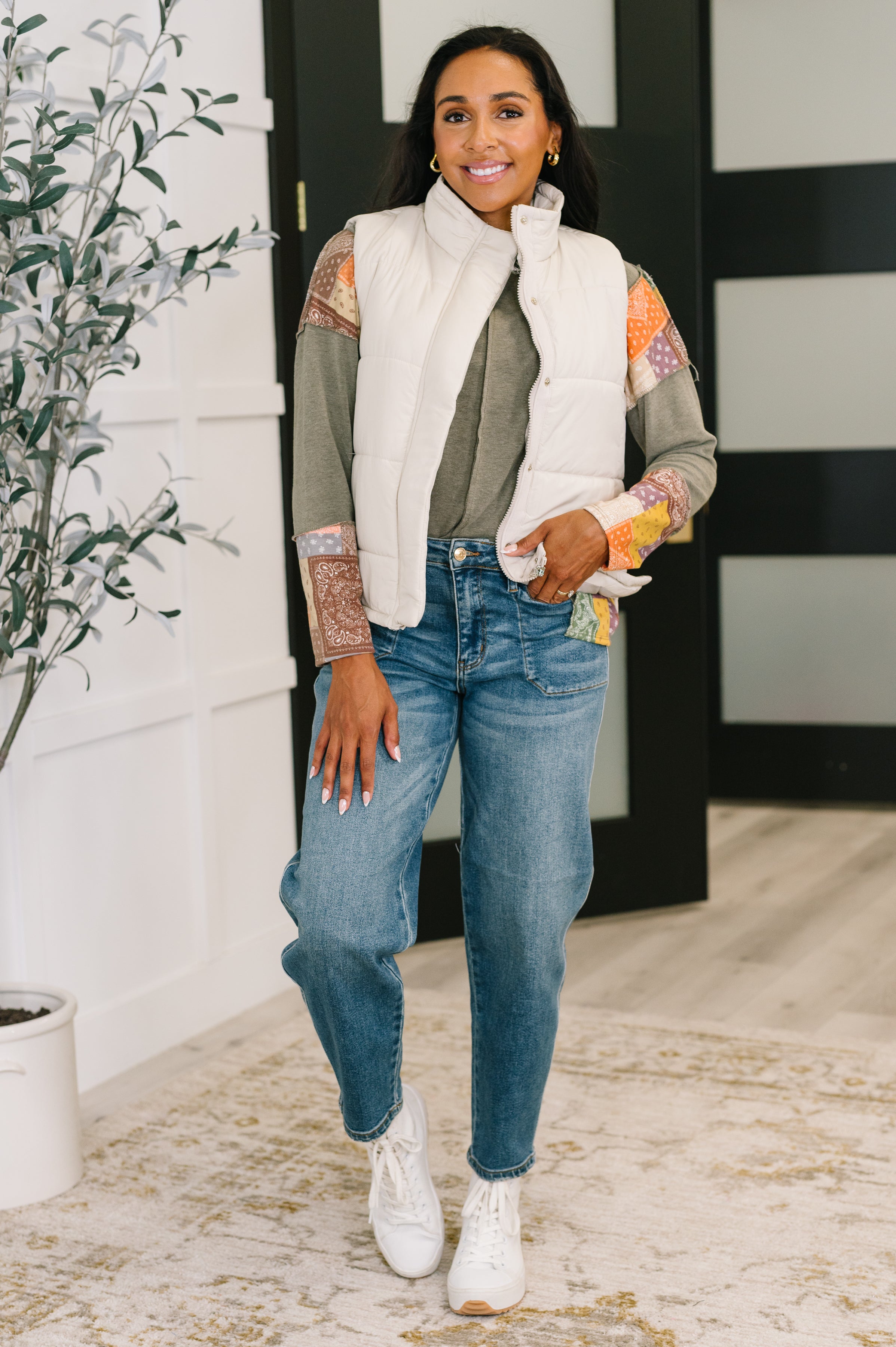 Woman wearing an olive color block relaxed long sleeve with high-waisted jeans and a light beige puffer vest indoors