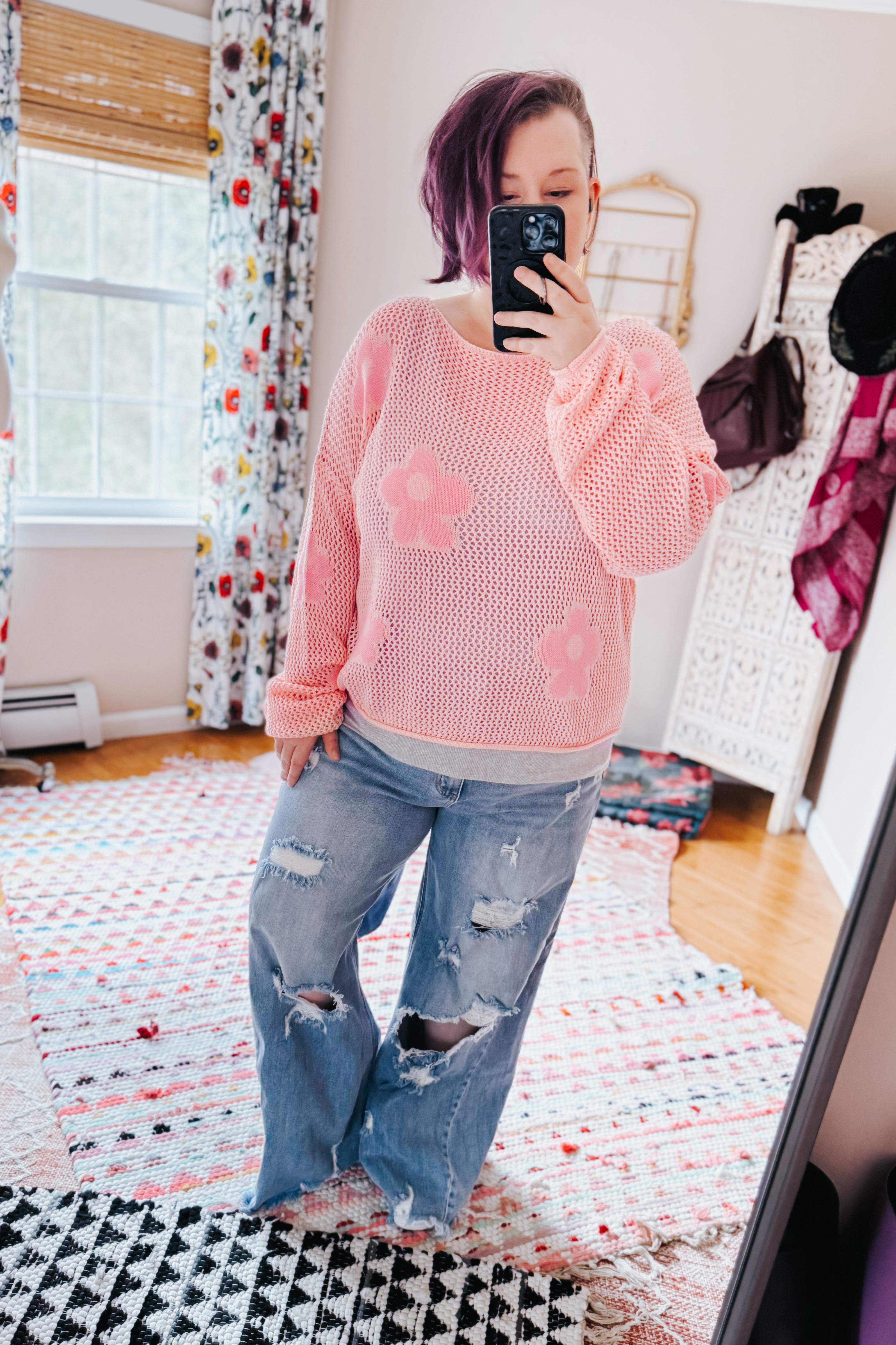 Woman wearing a blush pink floral mesh sweater top paired with distressed wide-leg jeans in a bright room with patterned rugs