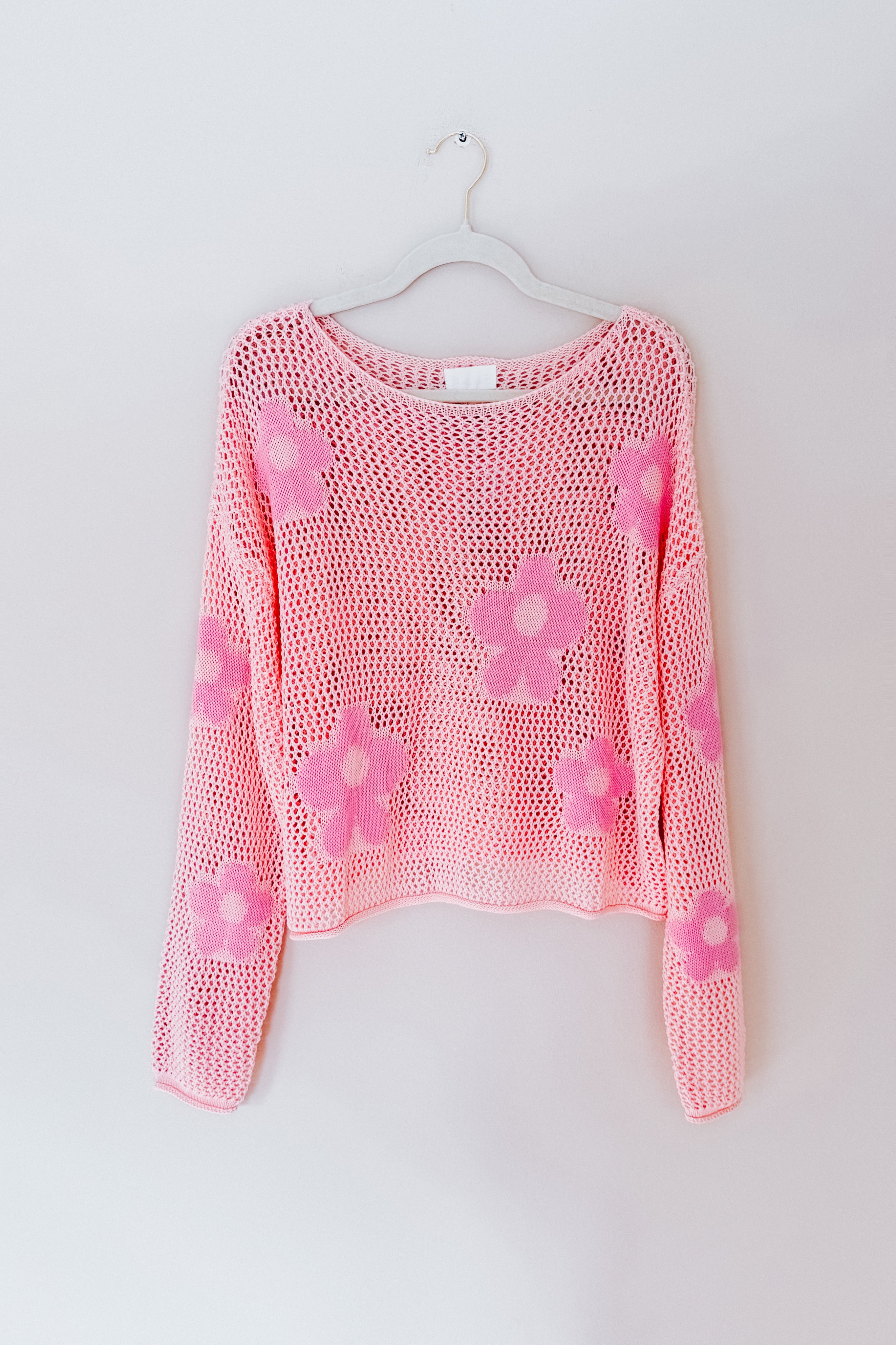 Light pink mesh sweater with bold pink floral patterns, designed with a loose and breathable fit on a hanger against a plain wall