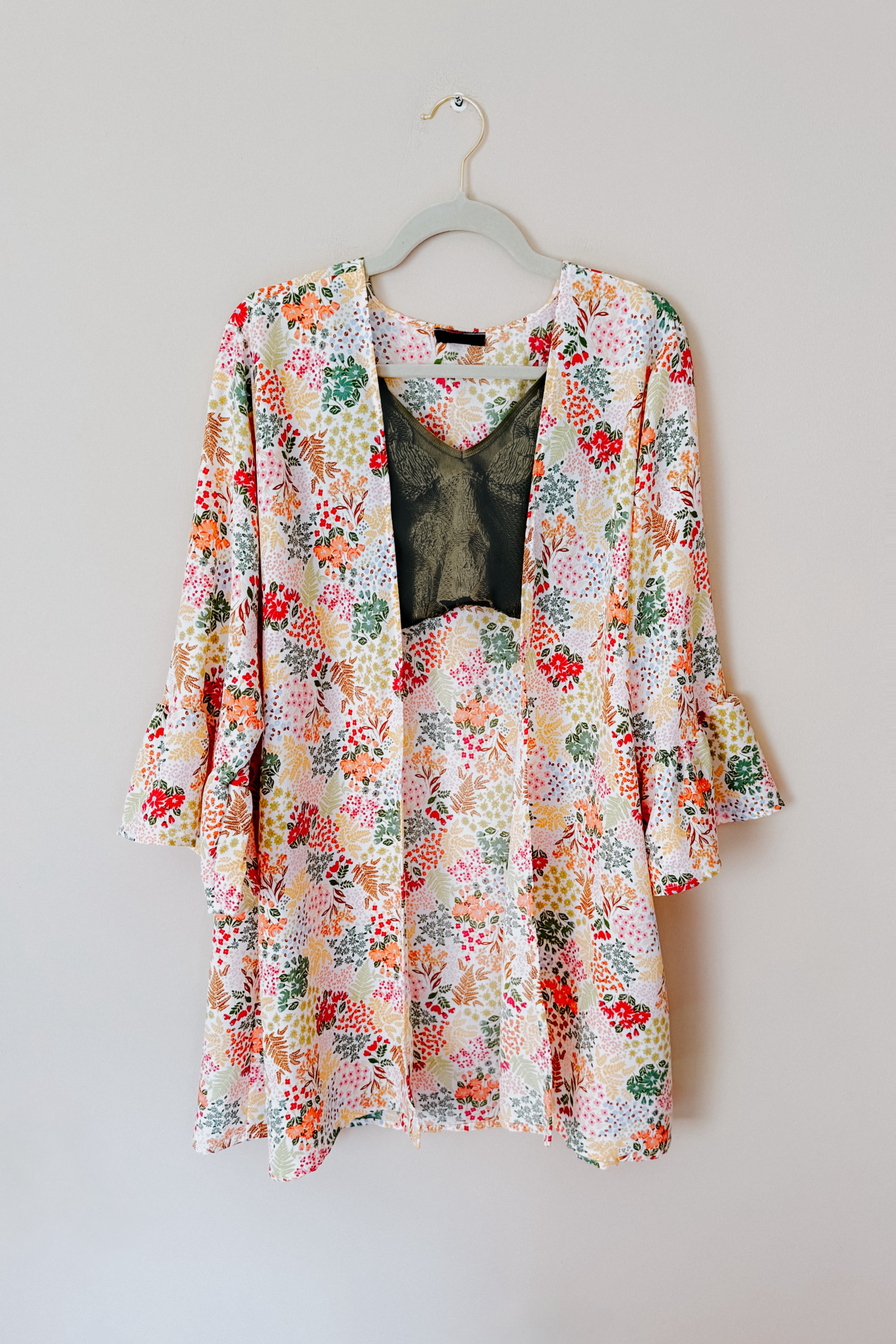 Ivory floral lightweight cardigan with ruffled sleeves layered over dark green lace camisole on a hanger