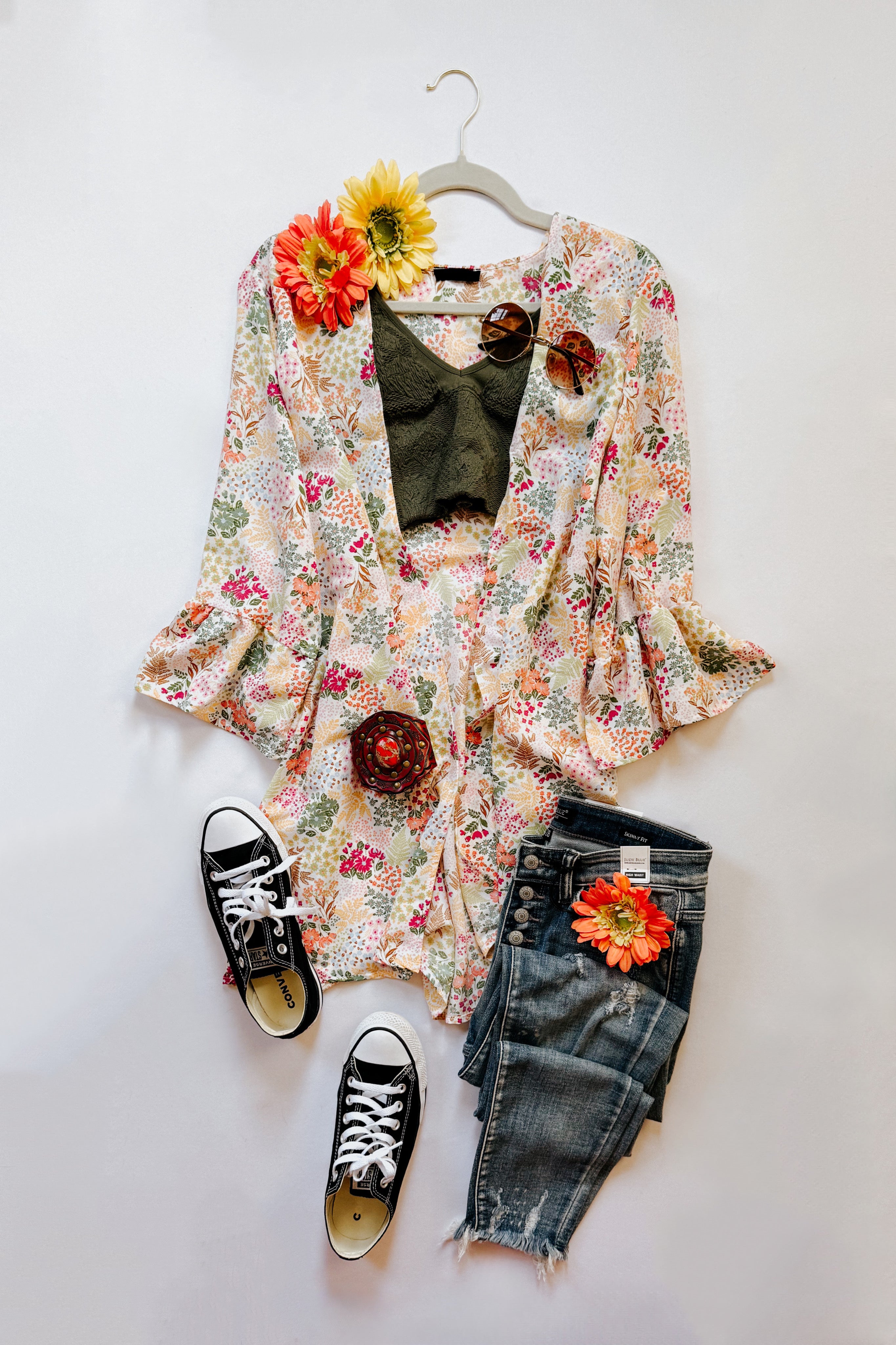 Ivory floral Sweet Bloom cardigan styled with olive top, distressed jeans, black sneakers, and floral accessories on white background
