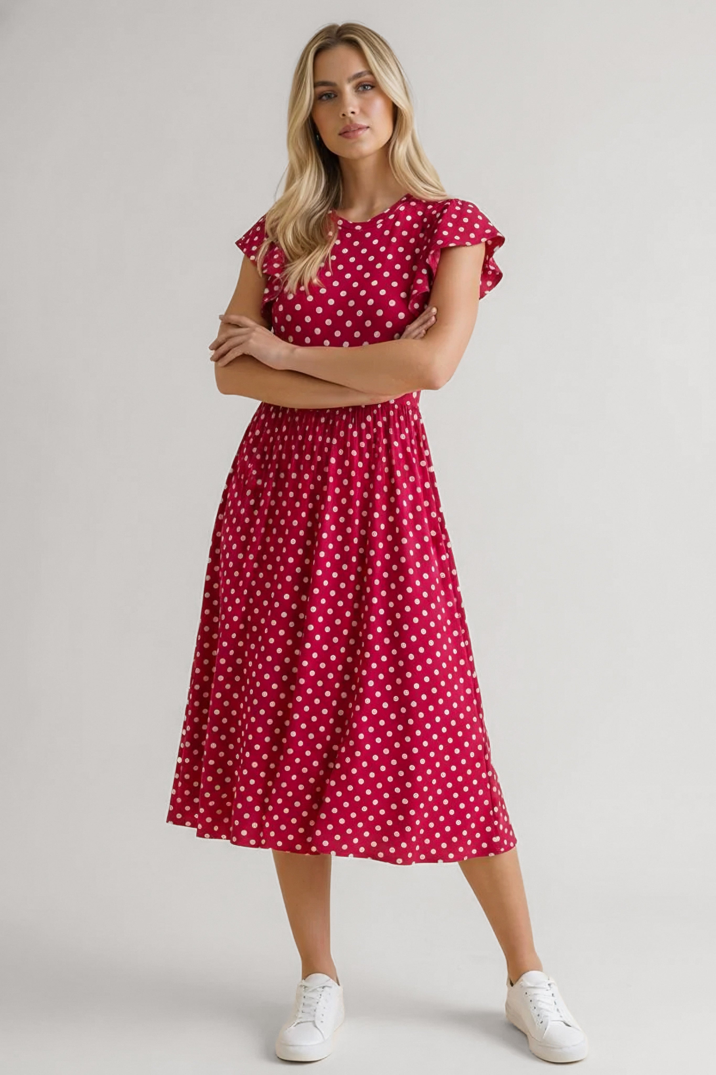 Woman wearing red polka dot midi dress with flutter sleeves standing confidently with arms crossed