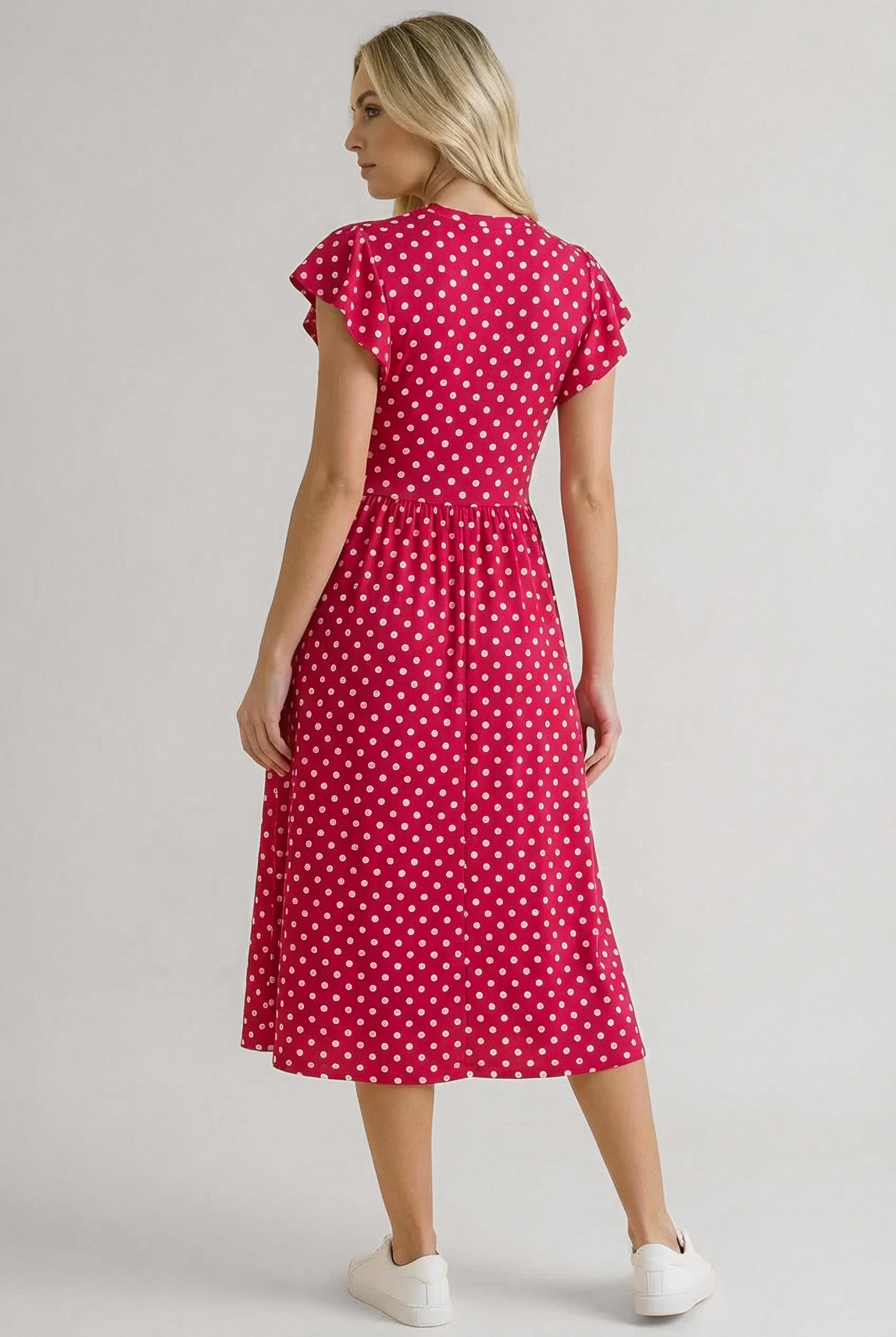 Woman wearing red polka dot midi dress with flutter sleeves and white sneakers, standing with back to camera
