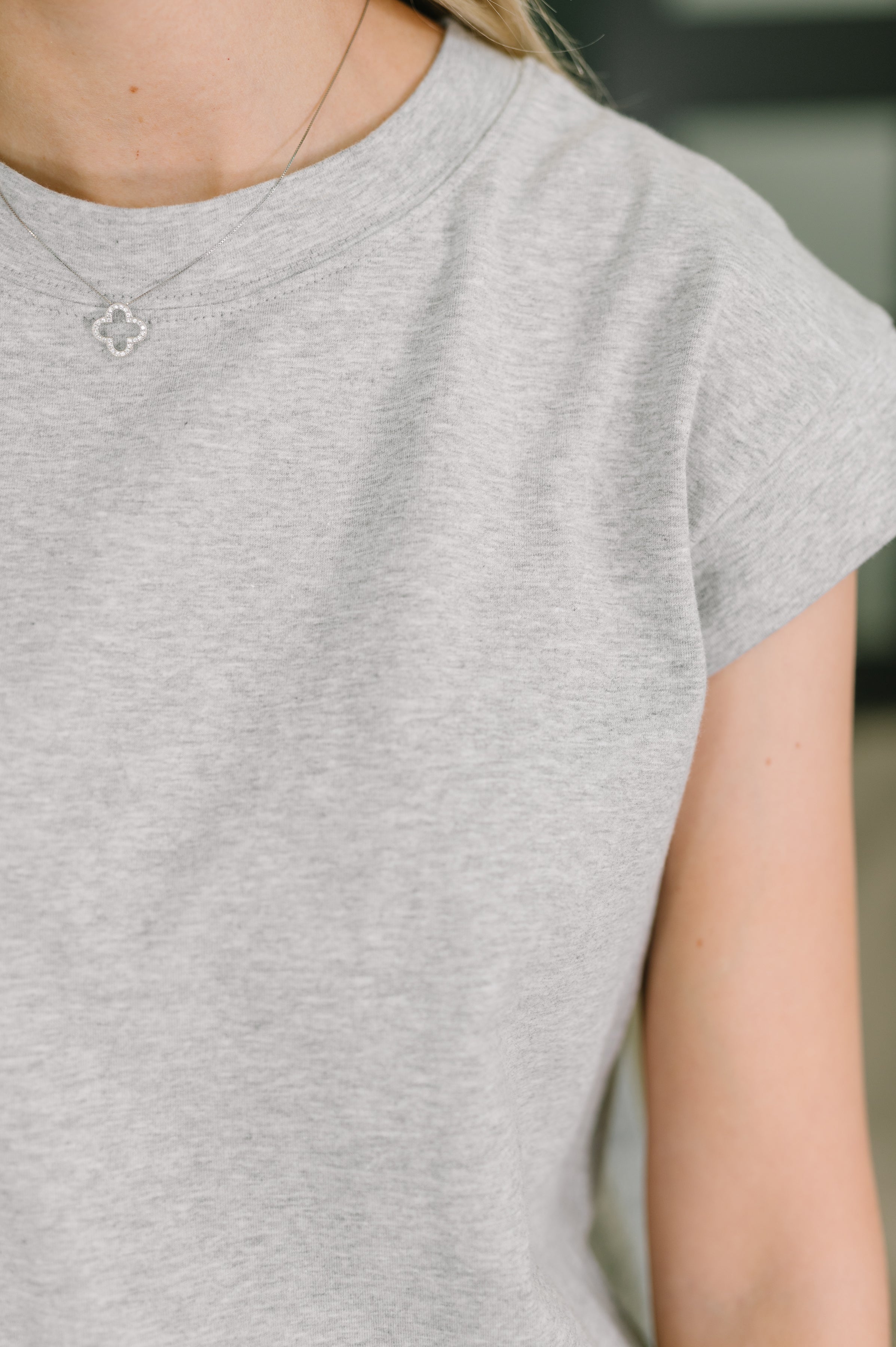 Close-up of heather grey casual dress fabric and sleeve worn with delicate silver clover pendant necklace