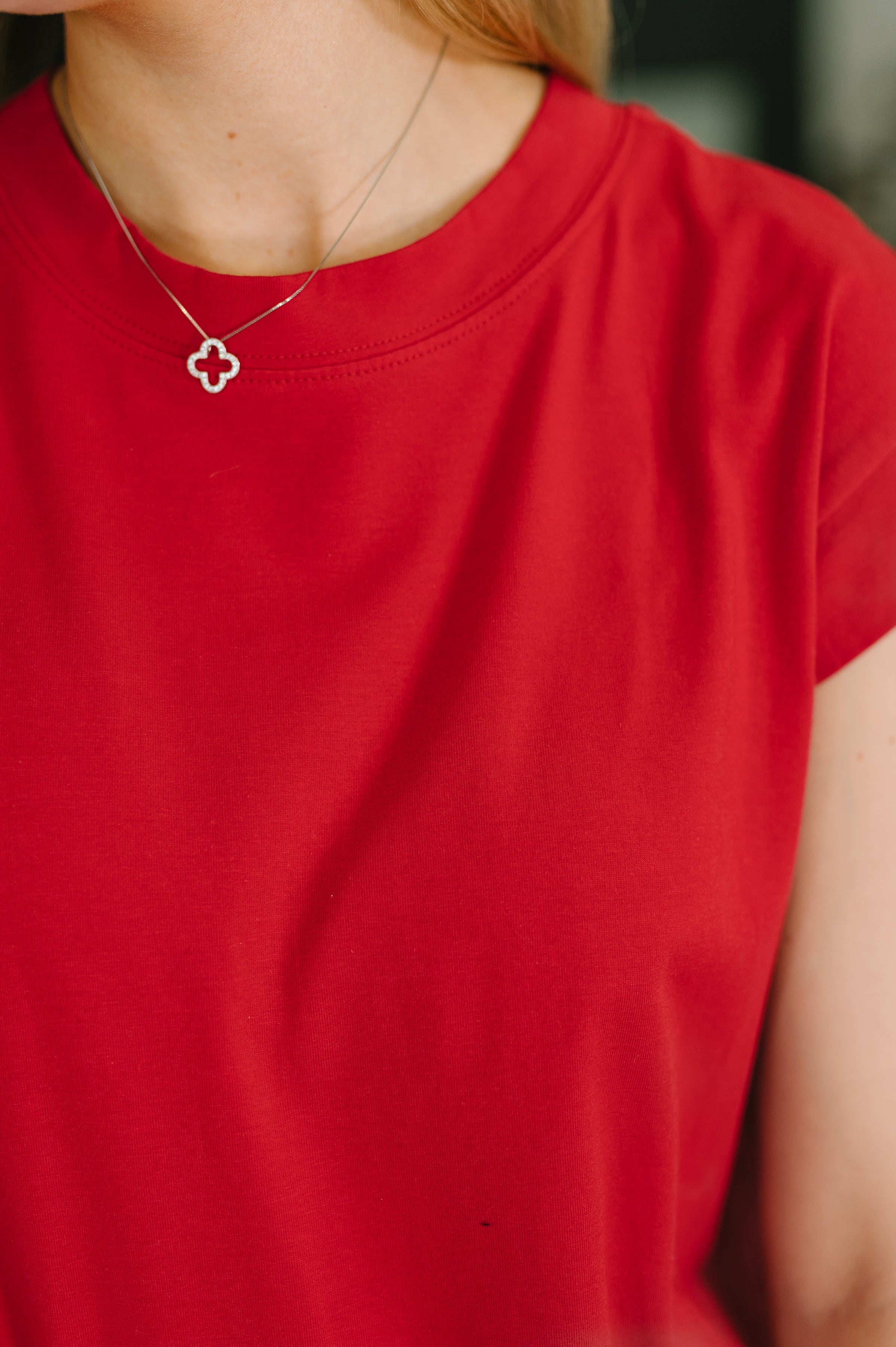 Close-up of vibrant ruby red casual dress fabric with delicate silver clover pendant necklace on model