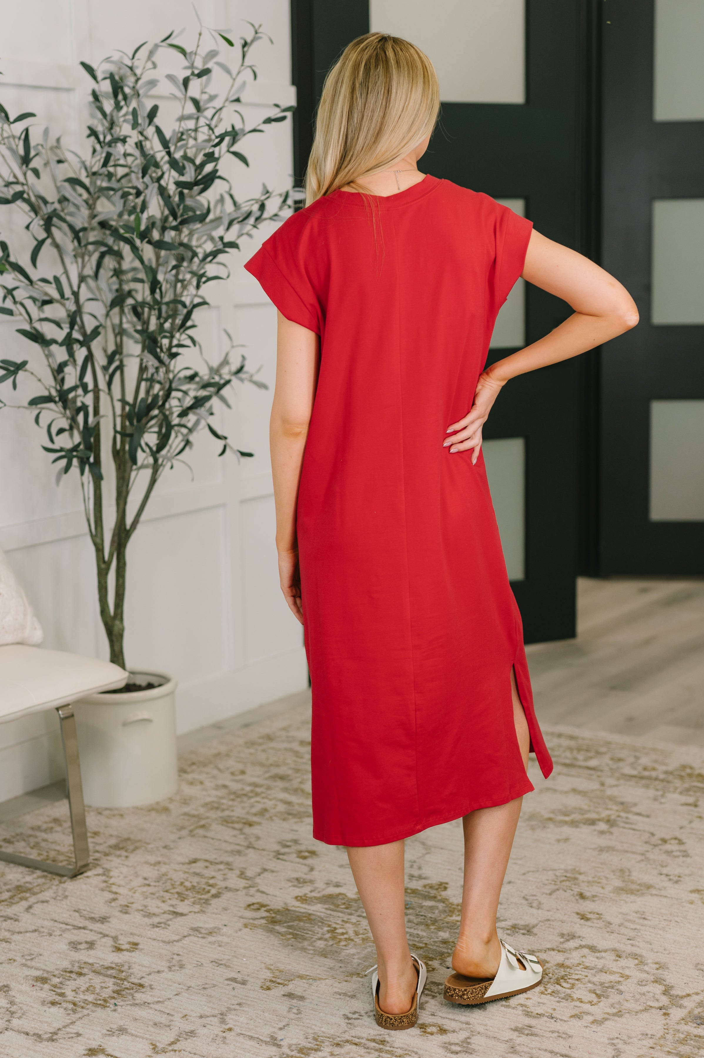 Woman wearing ruby red casual midi dress with short sleeves and side slit standing indoors on patterned rug