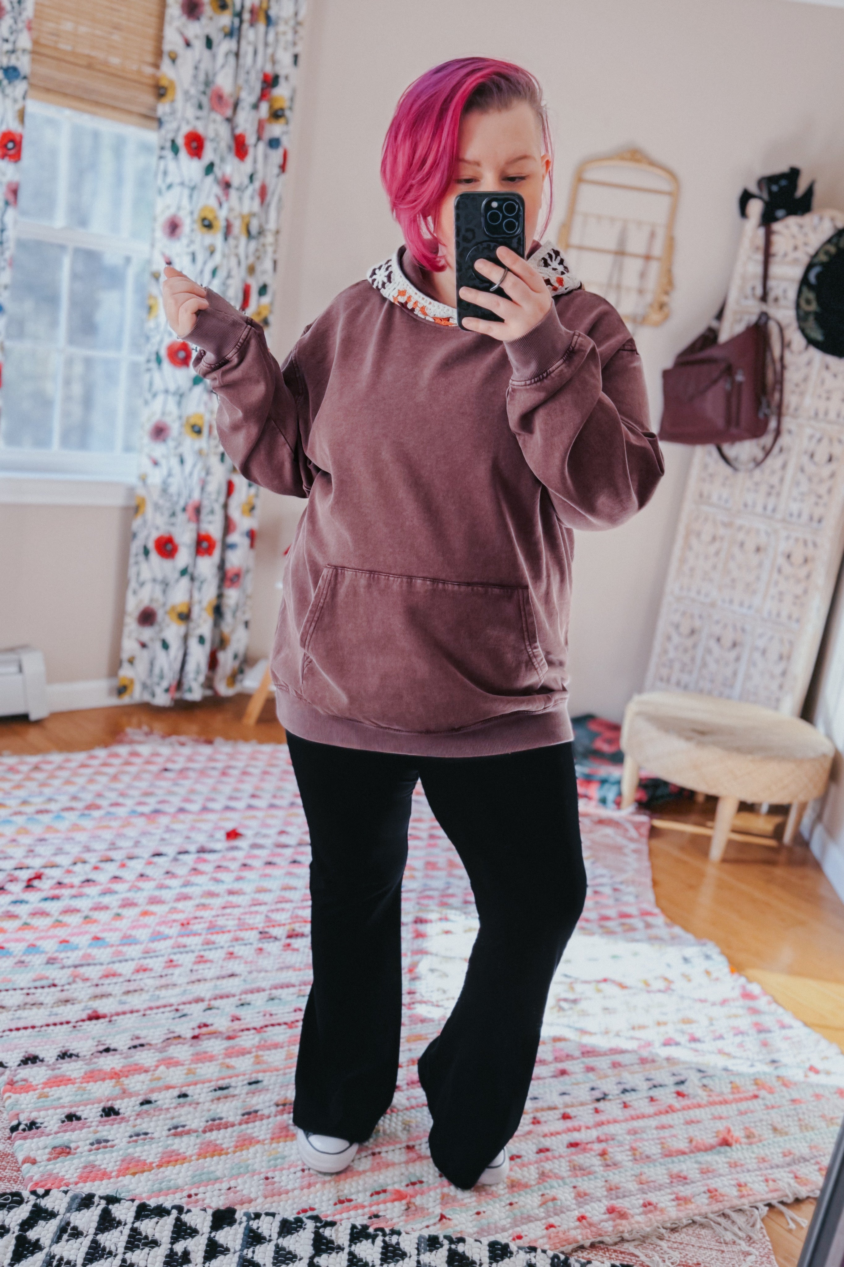 Woman taking a mirror selfie wearing an acid wash hoodie with crochet hood lining and black wide-leg pants indoors