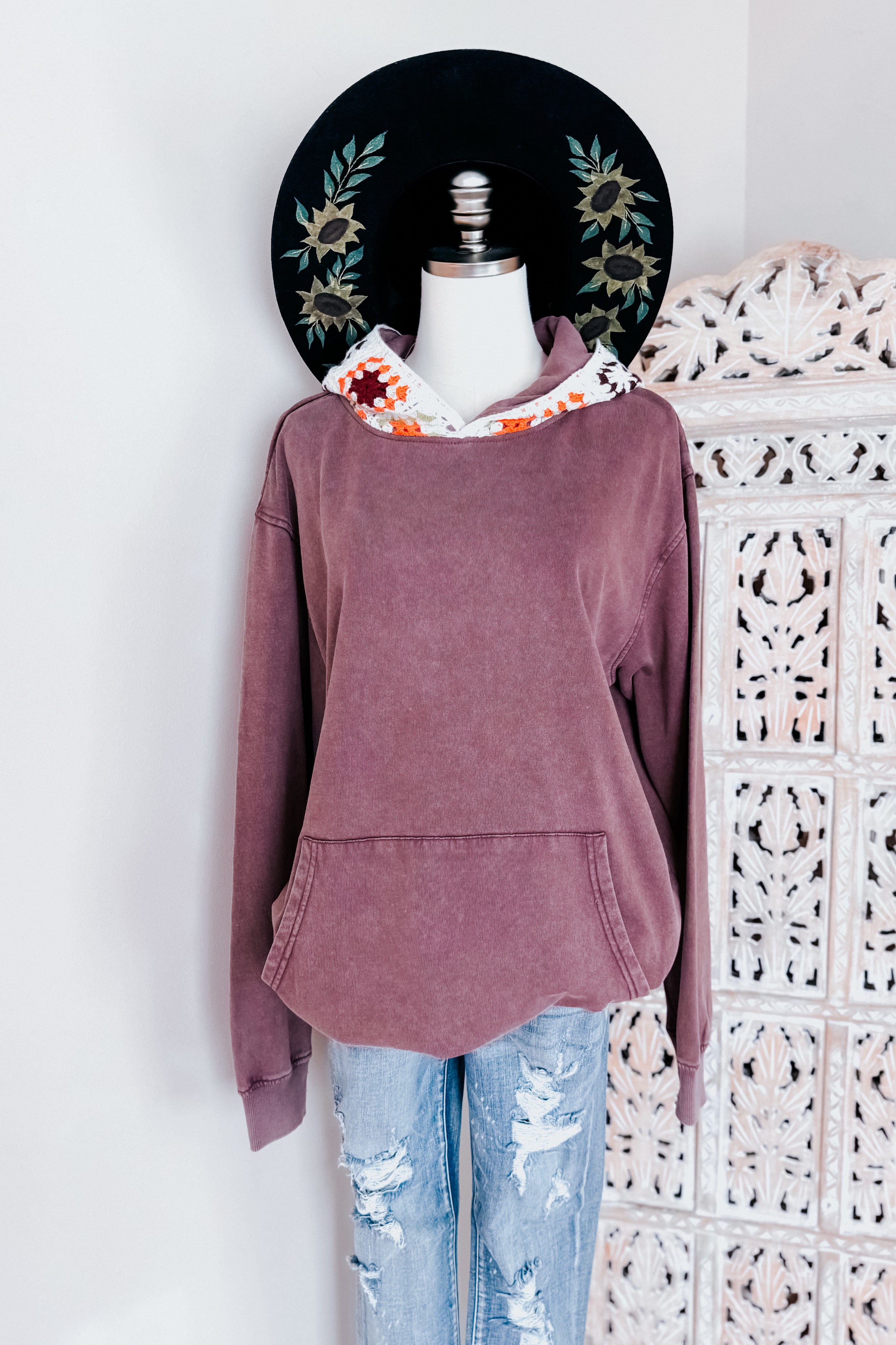 Purple acid wash hoodie with crochet hood lining styled with distressed light blue jeans on mannequin indoors