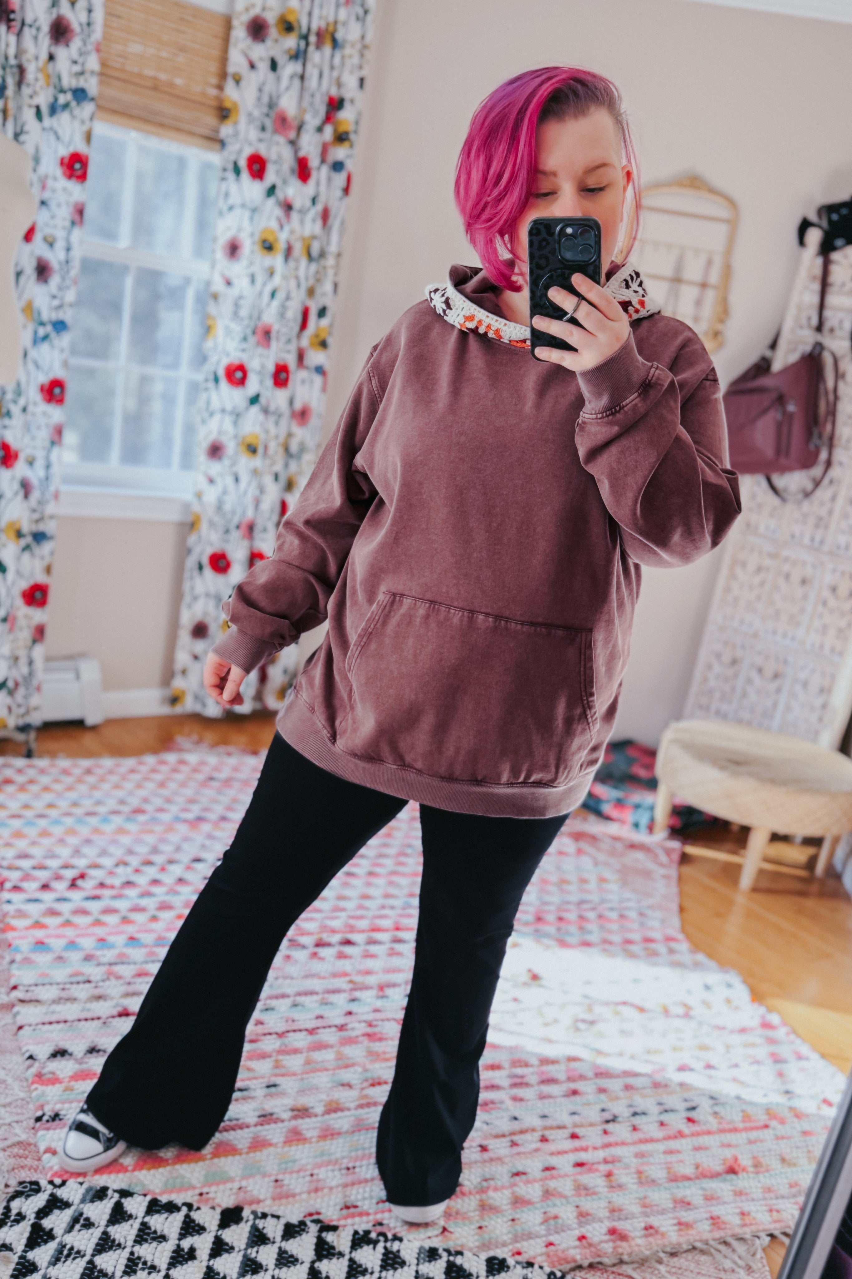 Woman with vibrant pink hair wearing a plush acid wash hoodie with floral hood lining and black flared pants indoors