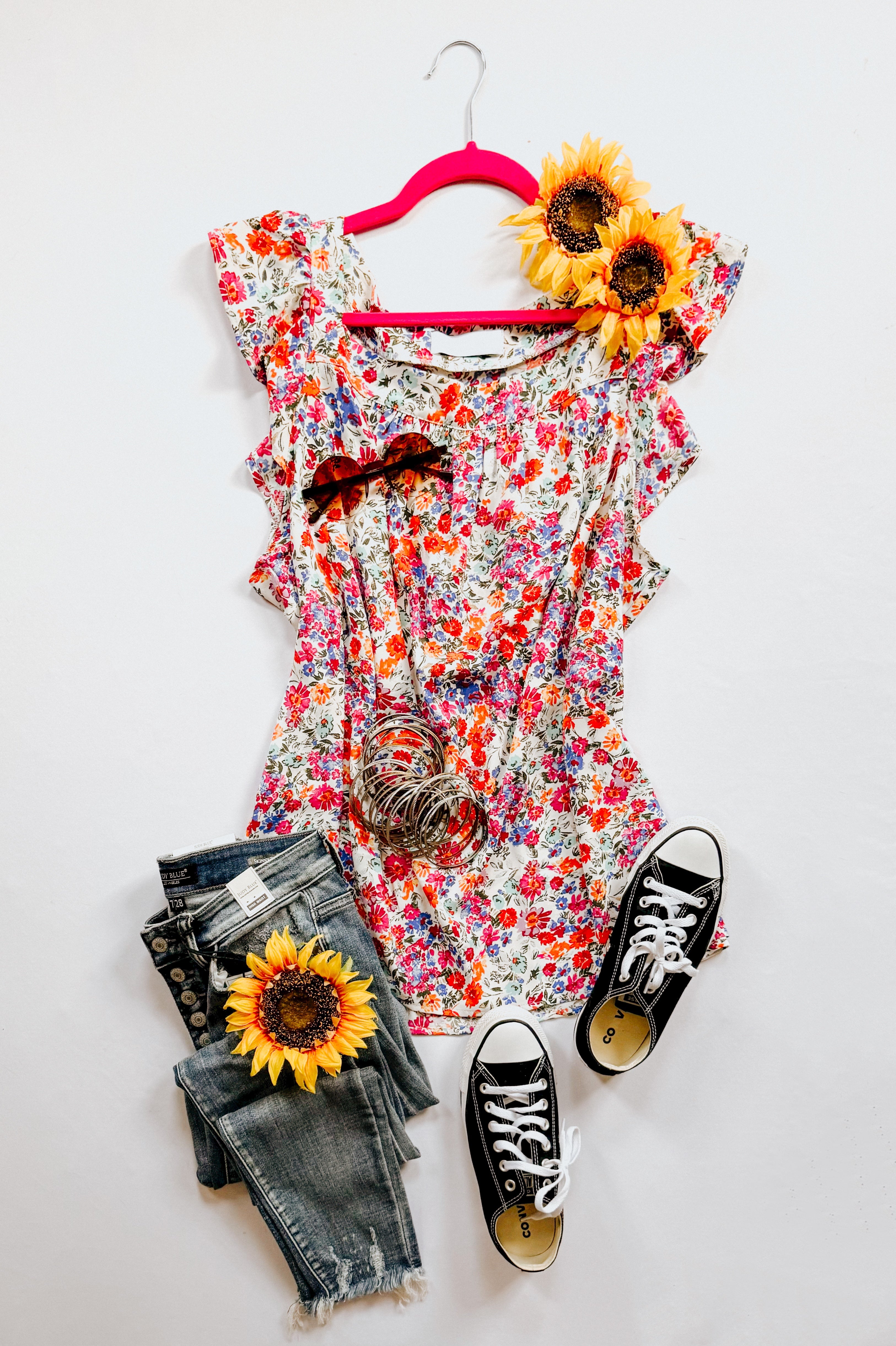 Red floral print top with ruffled sleeves on pink hanger styled with denim jeans, black sneakers, and sunflowers