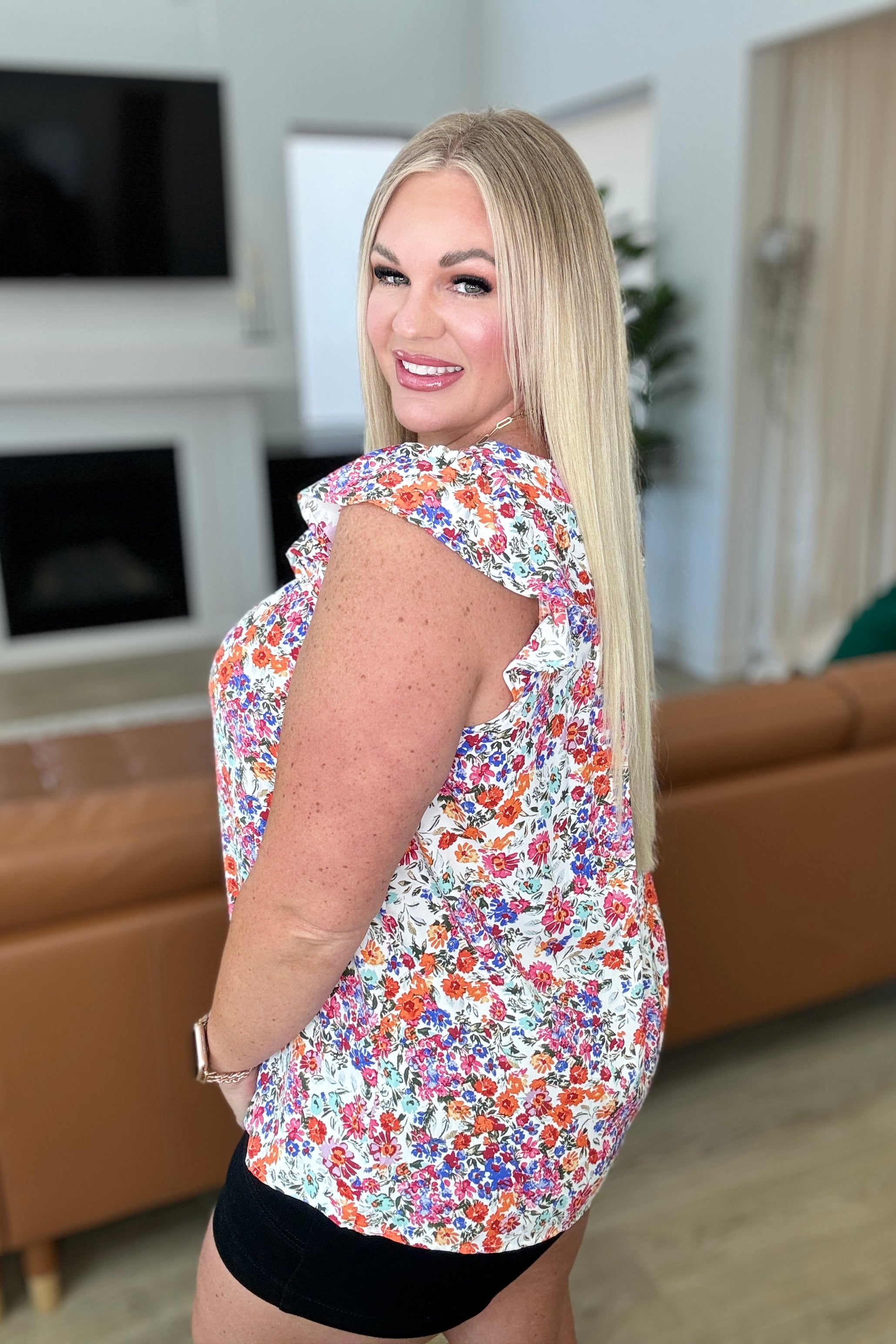 Curvy woman wearing a vibrant floral top with ruffled sleeves paired with black shorts in a cozy living room setting