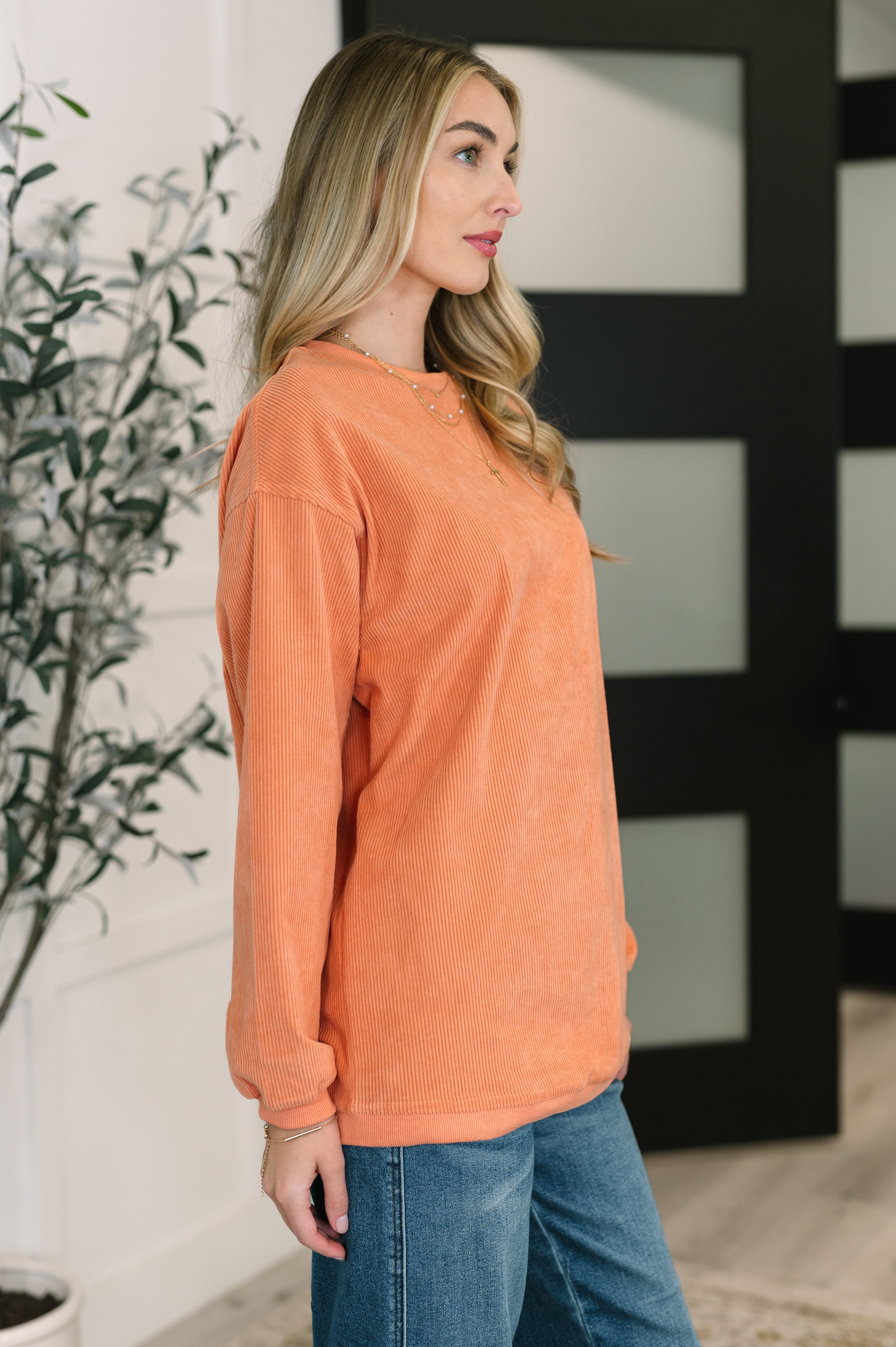 Woman wearing oversized orange corded sweatshirt paired with relaxed denim jeans in modern indoor setting