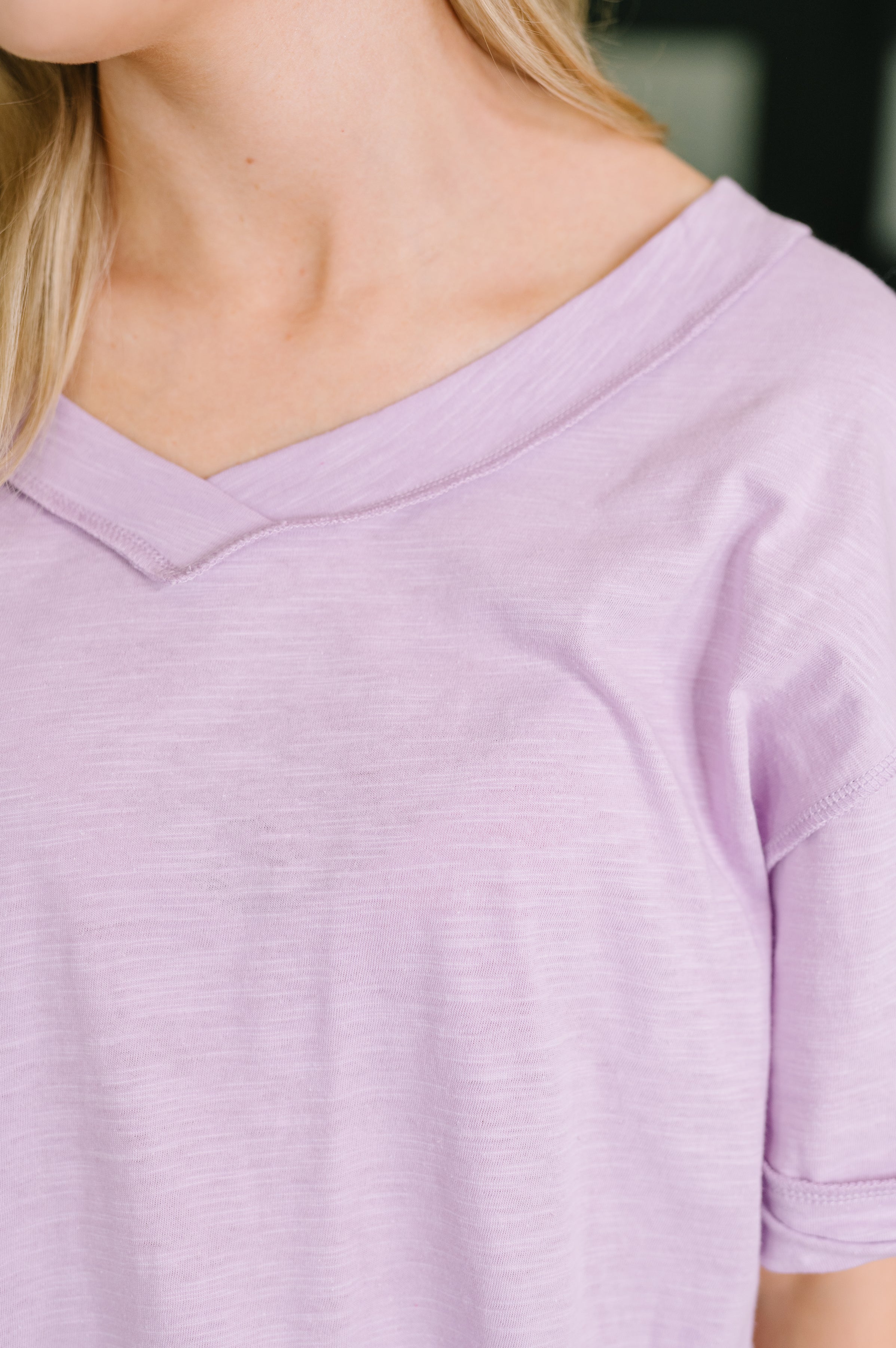 Close-up of soft lilac relaxed tee with banded V-neck and subtle heathered texture on model’s upper torso