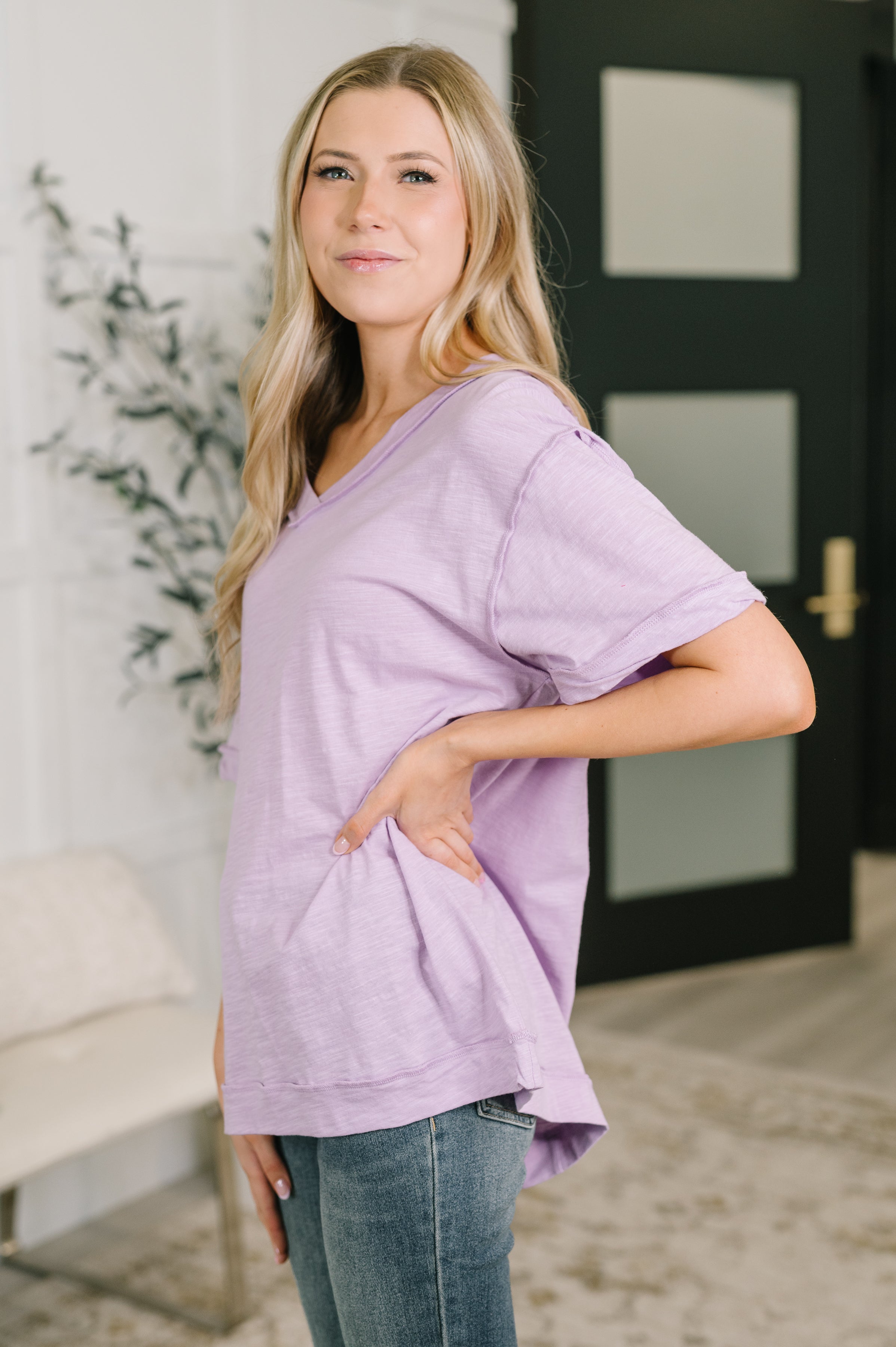 Woman wearing lilac relaxed fit V-neck tee with rolled sleeves and casual jeans in bright modern indoor space
