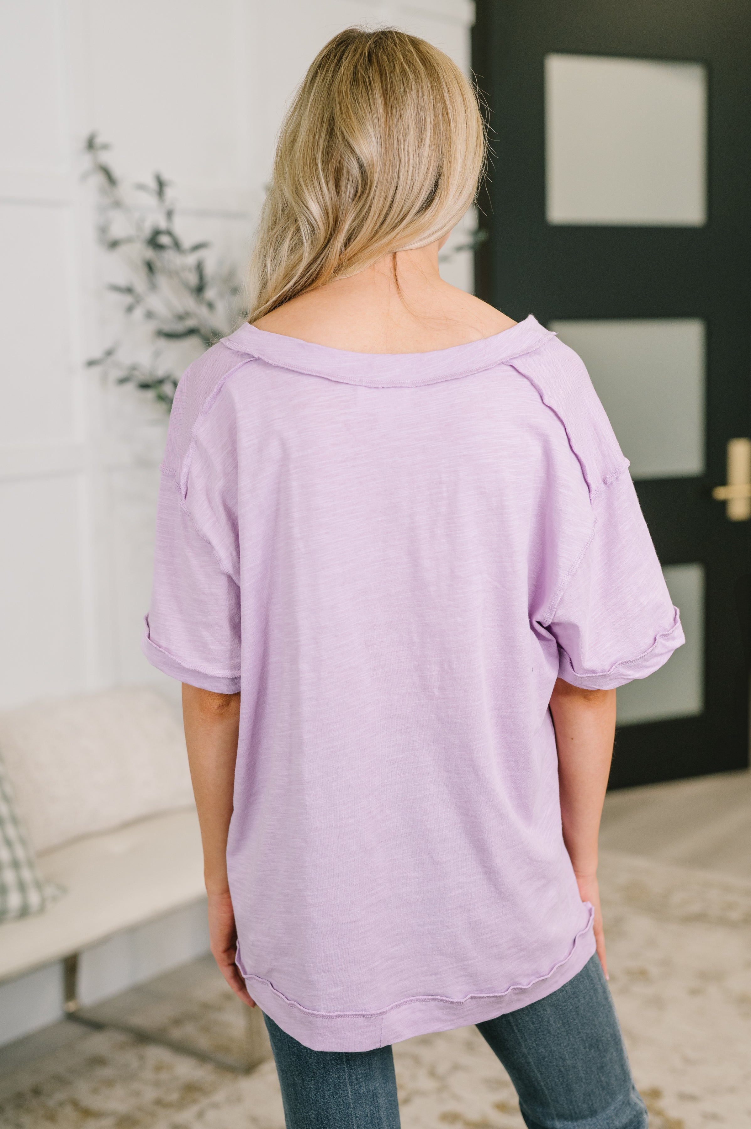 Back view of woman wearing lilac relaxed tee with rolled sleeves in casual cozy indoor setting