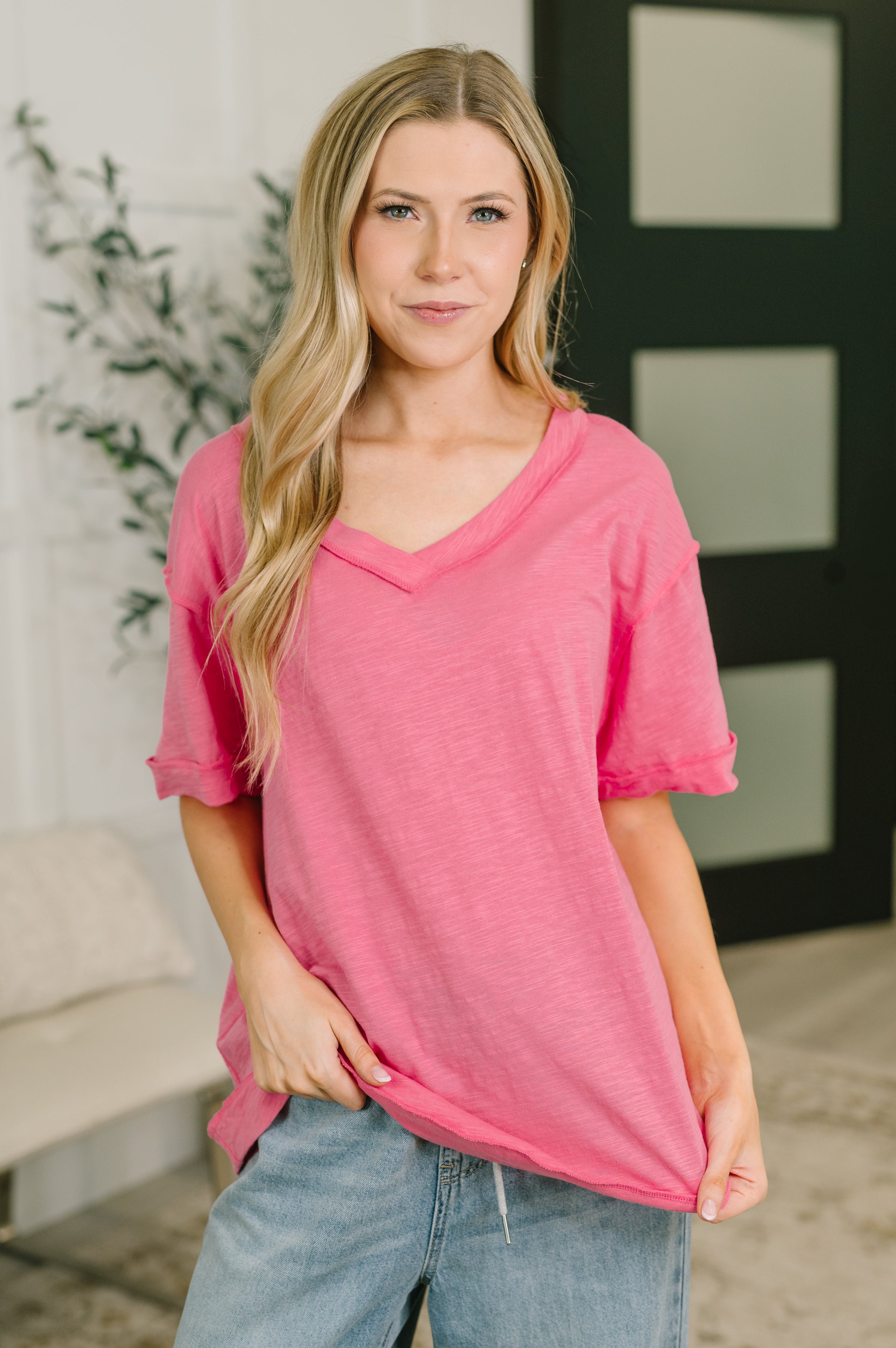 Woman in pink relaxed V-neck short sleeve tee with soft texture paired with light wash denim in casual indoor setting