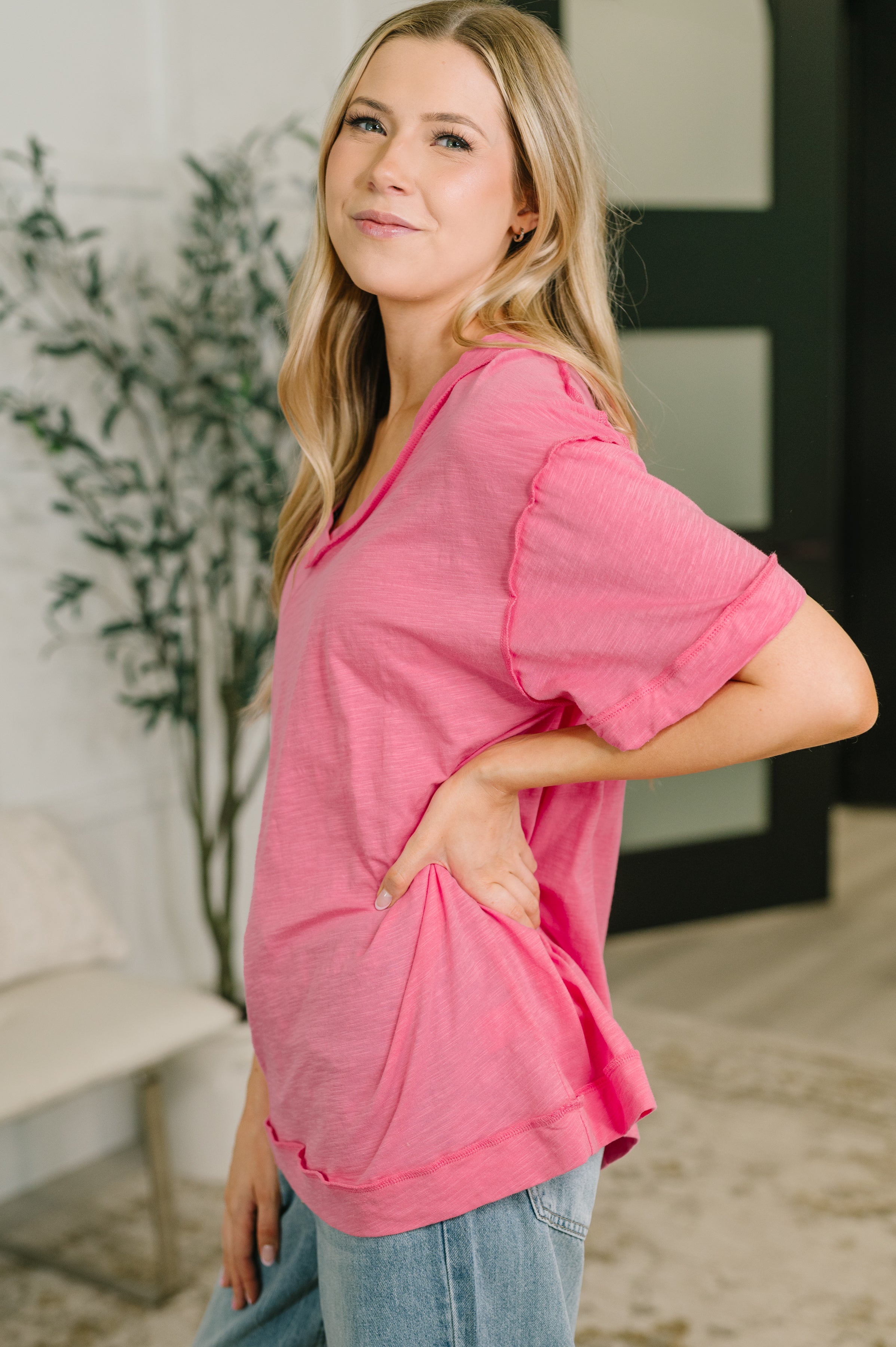 Side view of woman in relaxed pink V-neck tee with subtle texture and soft fabric paired with casual light-wash denim jeans