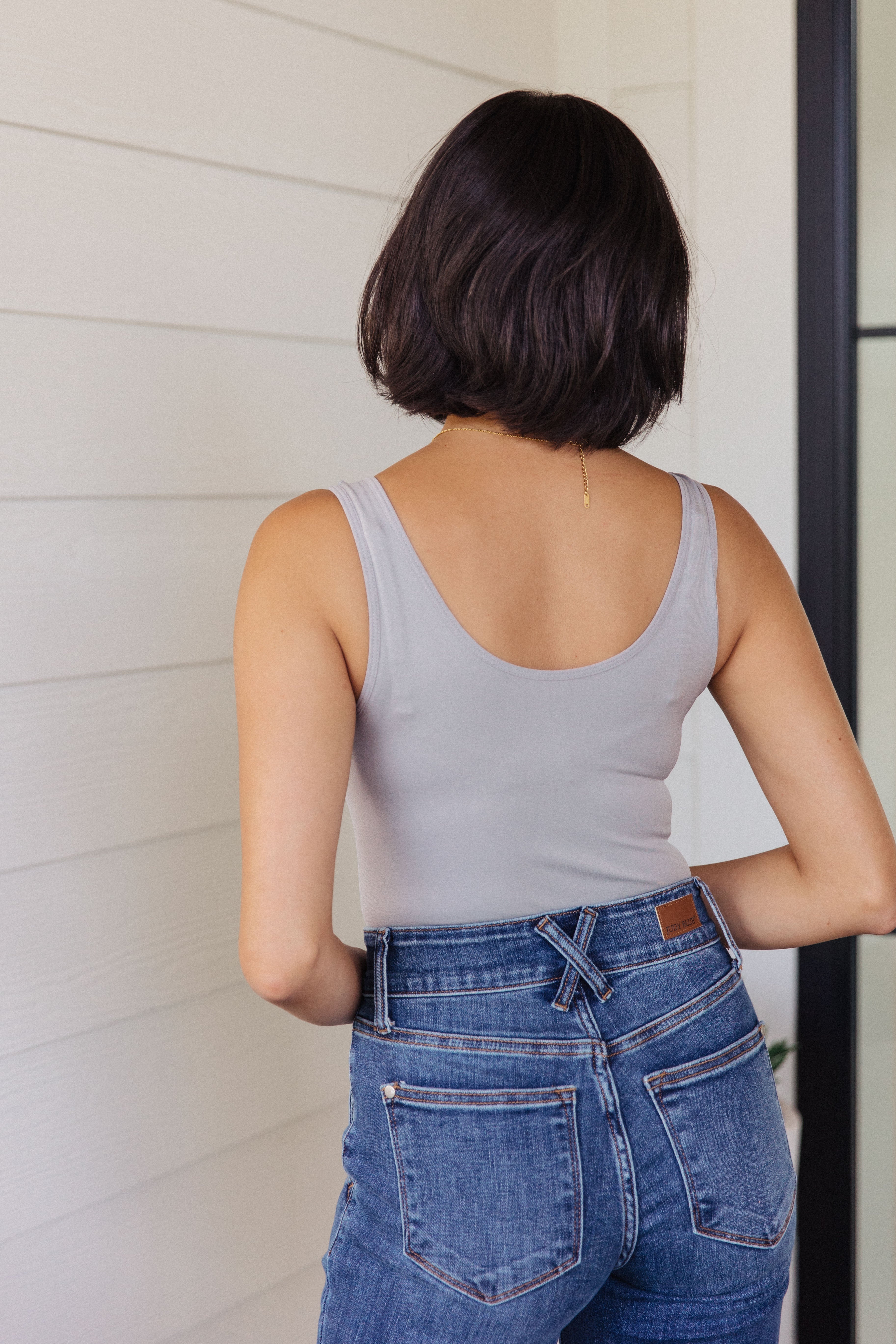 Woman with short dark hair wearing a grey sleeveless fitted top and high-rise blue jeans seen from the back