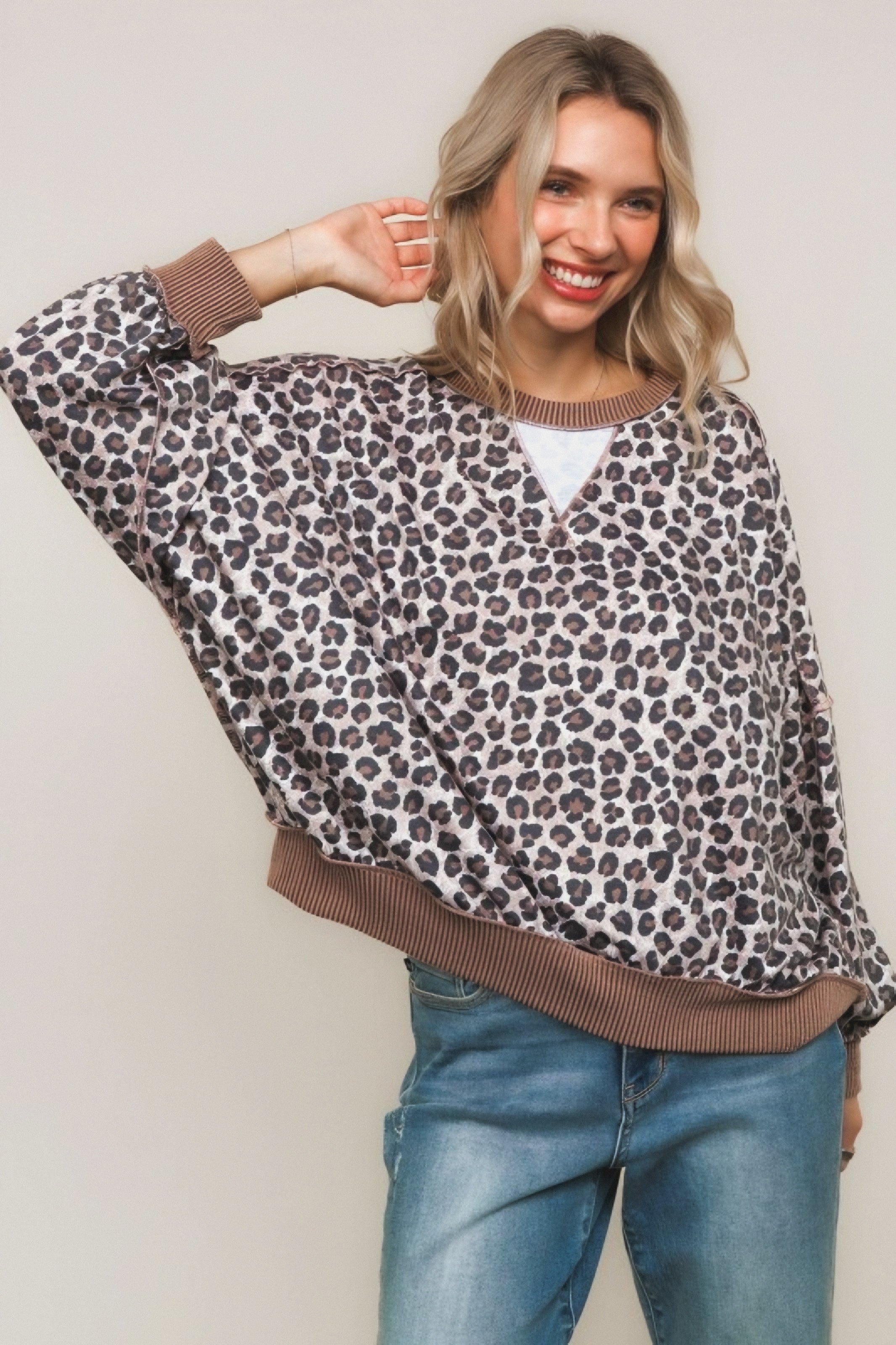Smiling woman wearing brown leopard print pullover with ribbed cuffs and hem paired with blue jeans against a neutral background