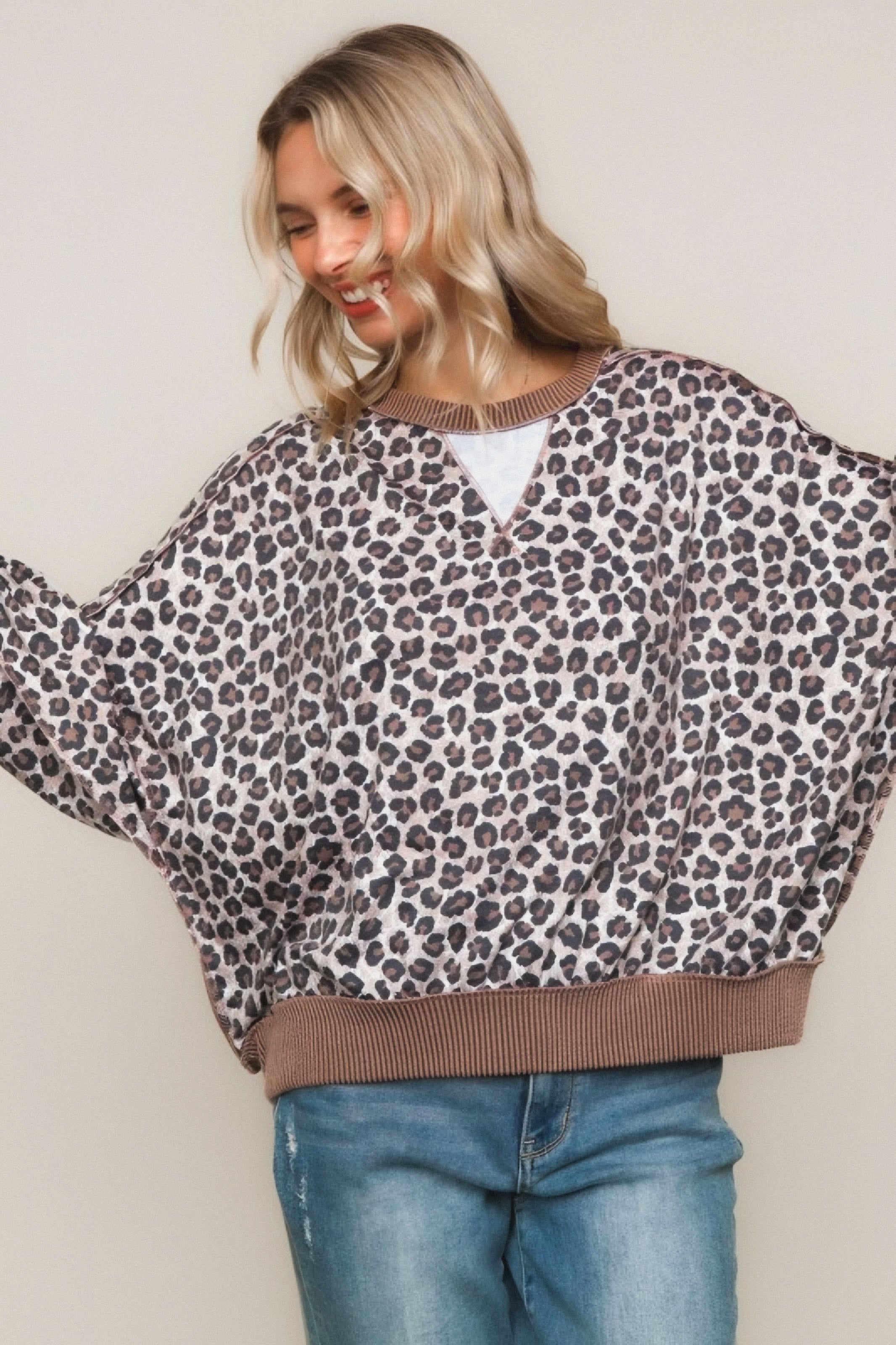 Woman smiling wearing a brown leopard print pullover with ribbed hem and collar paired with light wash jeans