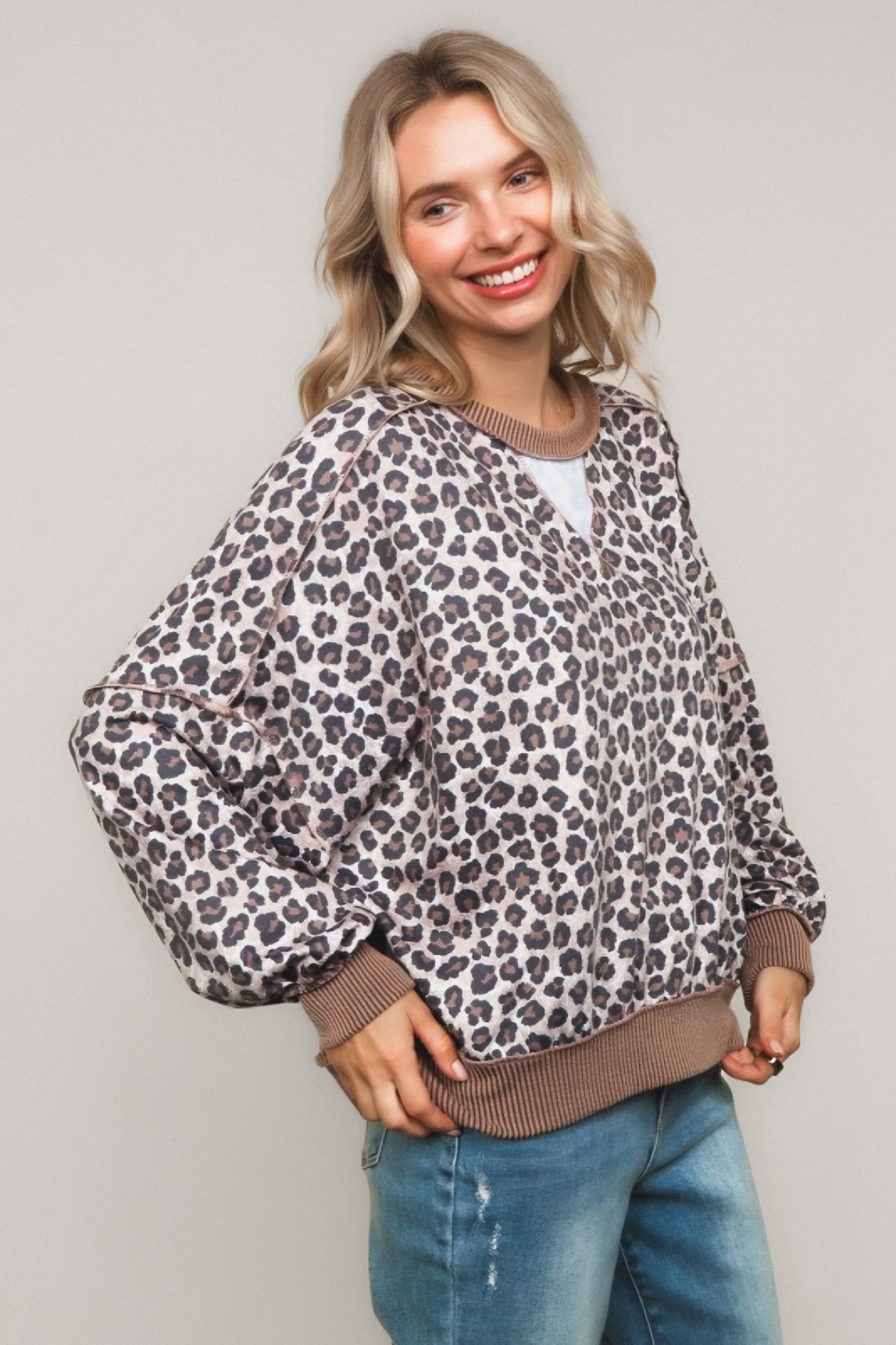 Smiling woman wearing a leopard print pullover with brown ribbed cuffs and hem paired with relaxed jeans