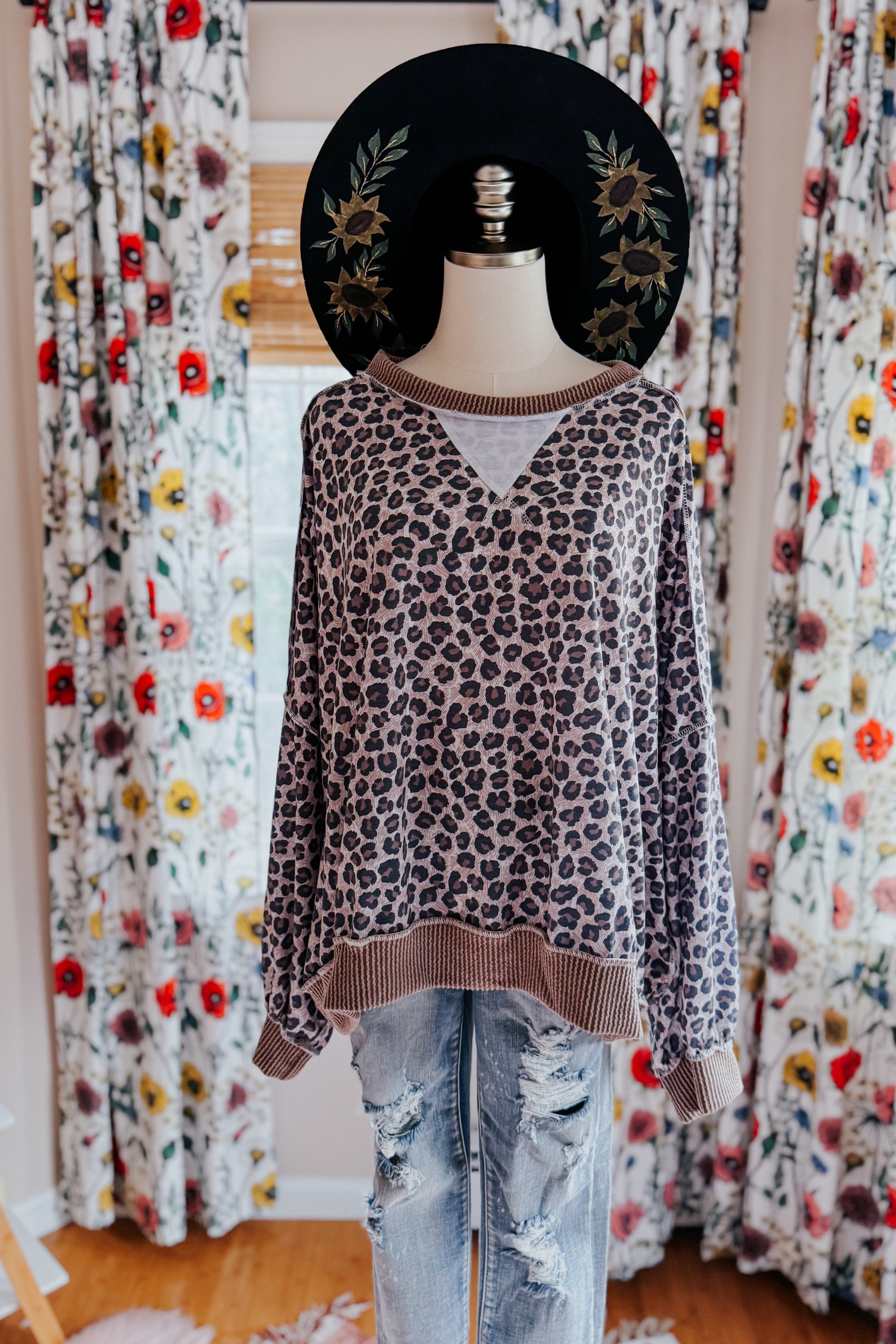 Mannequin wearing brown leopard print pullover with ribbed hem and distressed light blue jeans against floral curtains