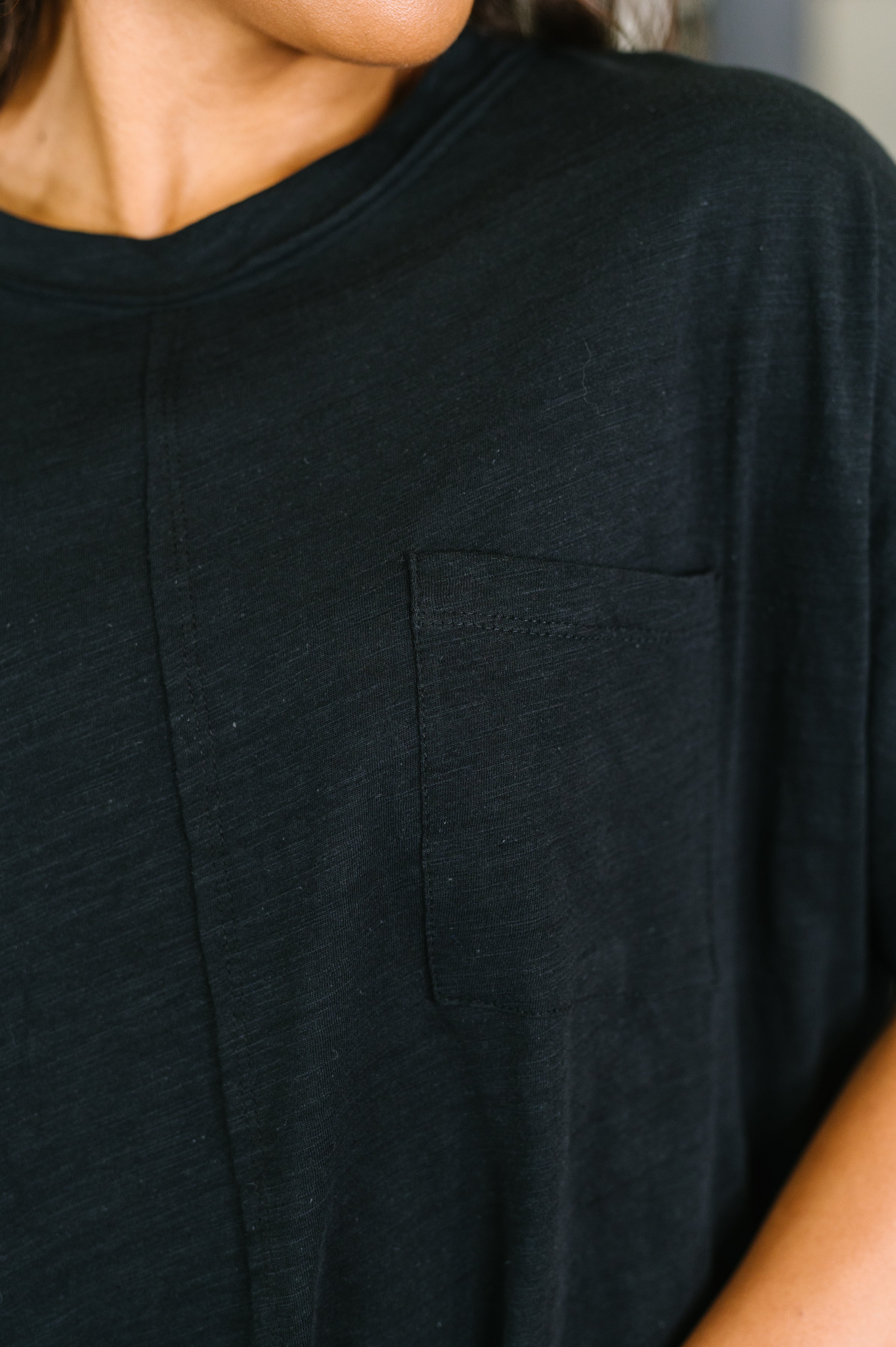 Close-up of black relaxed fit tee with crew neck and small chest pocket on model's upper torso