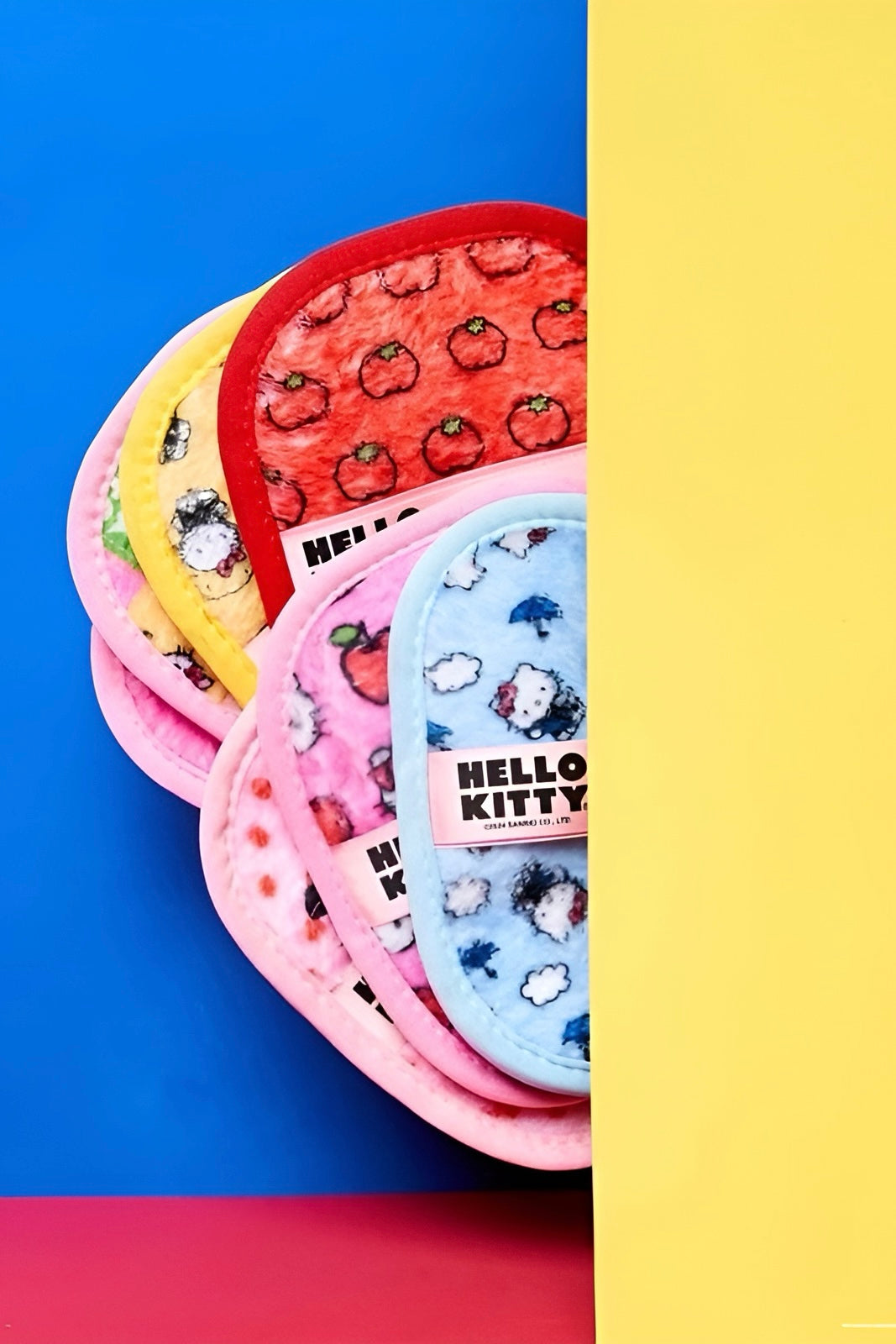 Assorted colorful Hello Kitty makeup eraser cloths with playful prints against a vibrant two-tone yellow and blue backdrop