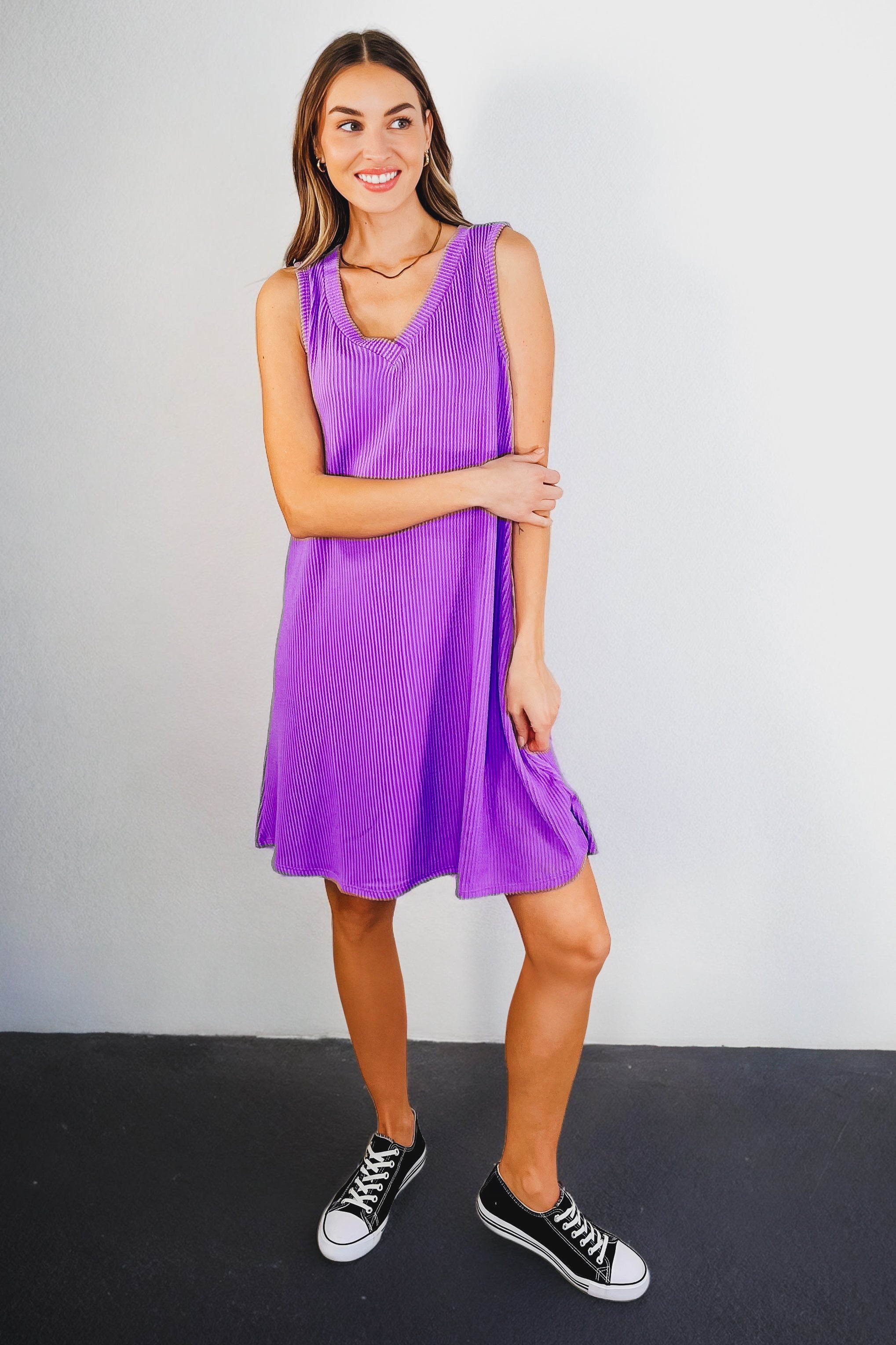 Woman wearing a tropical violet ribbed knit sleeveless dress paired with black low-top sneakers on dark floor