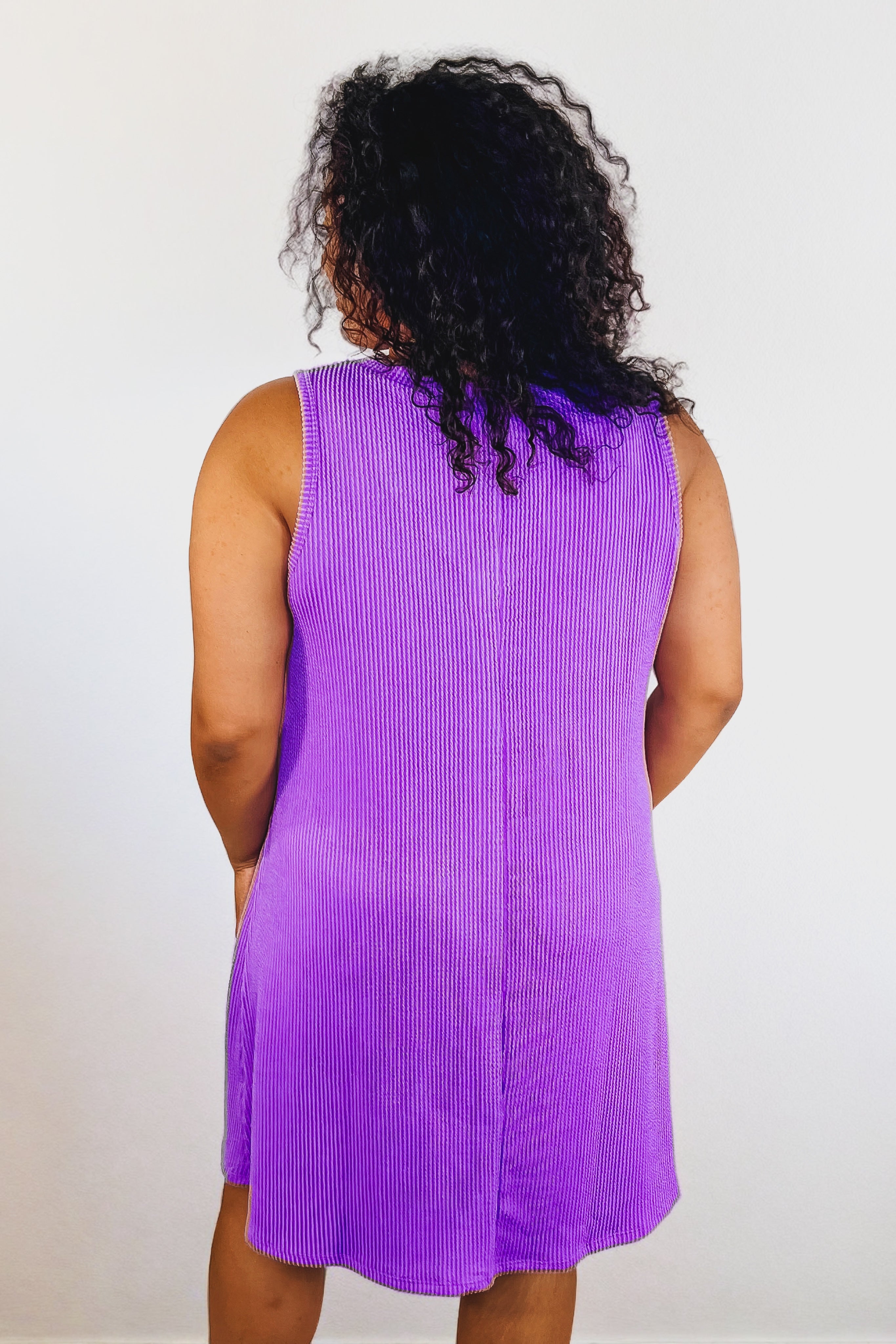 Plus-size model wearing a tropical violet sleeveless ribbed knit dress, shown from the back against a plain background