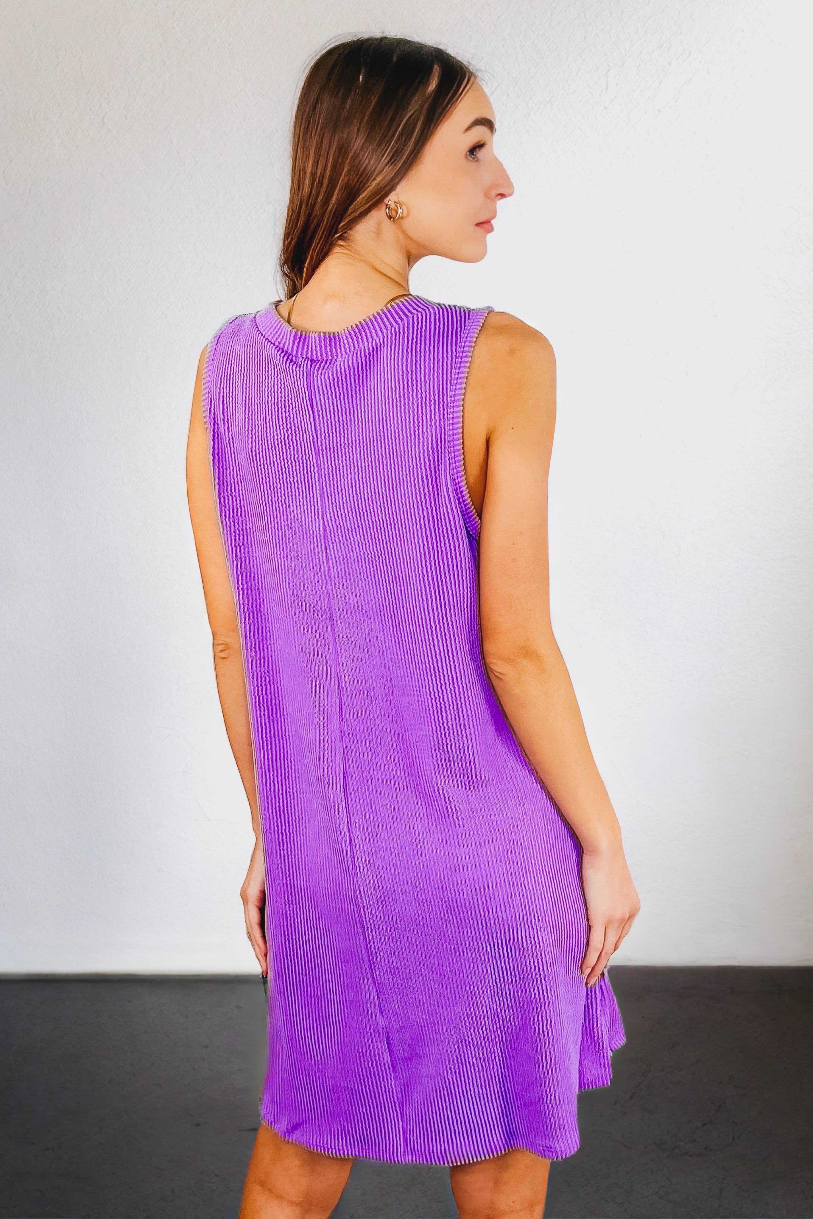 Woman wearing a tropical violet sleeveless ribbed knit dress with a relaxed fit, viewed from the back against white wall