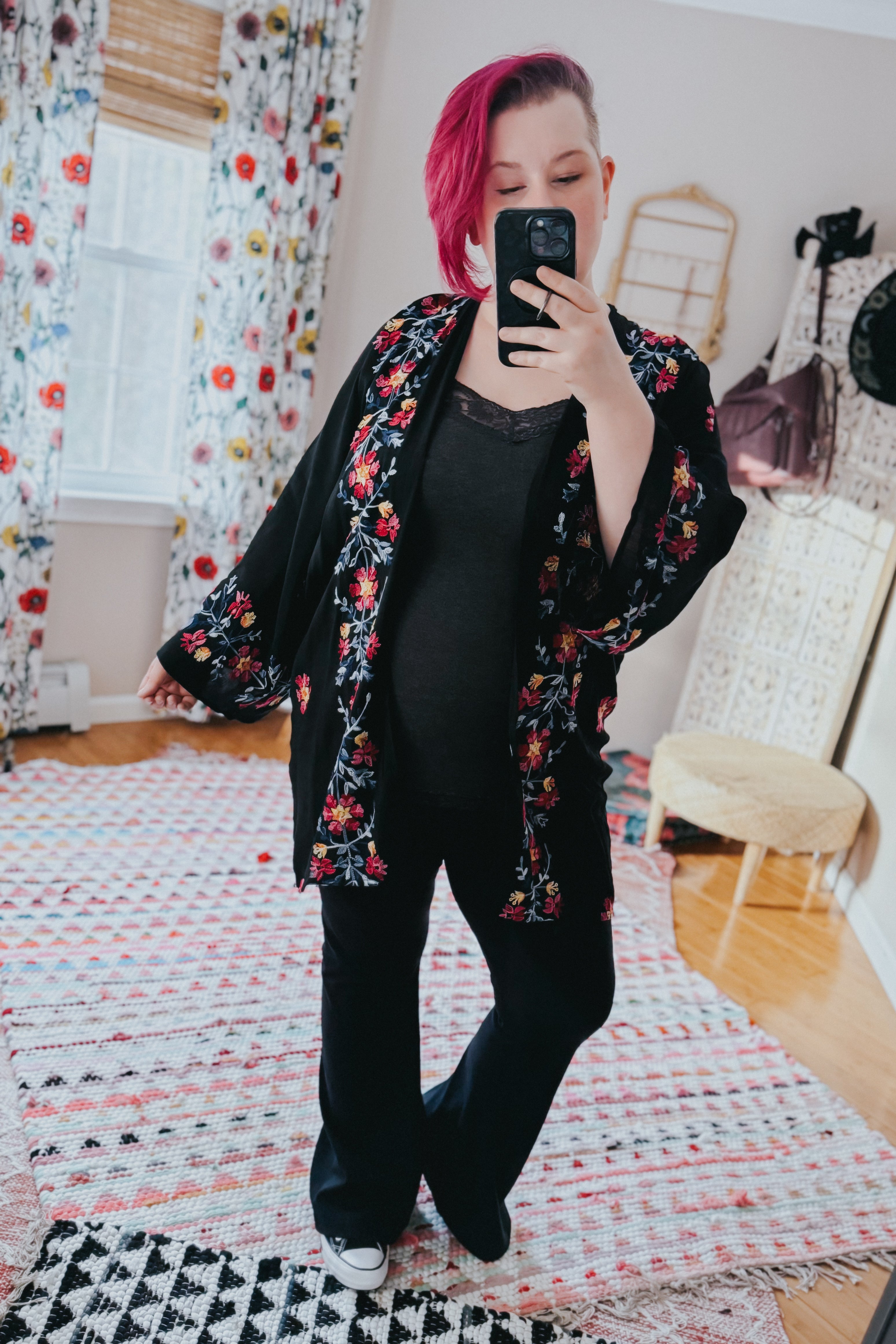 Woman wearing black embroidered bohemian duster with floral details and black outfit taking mirror selfie indoors