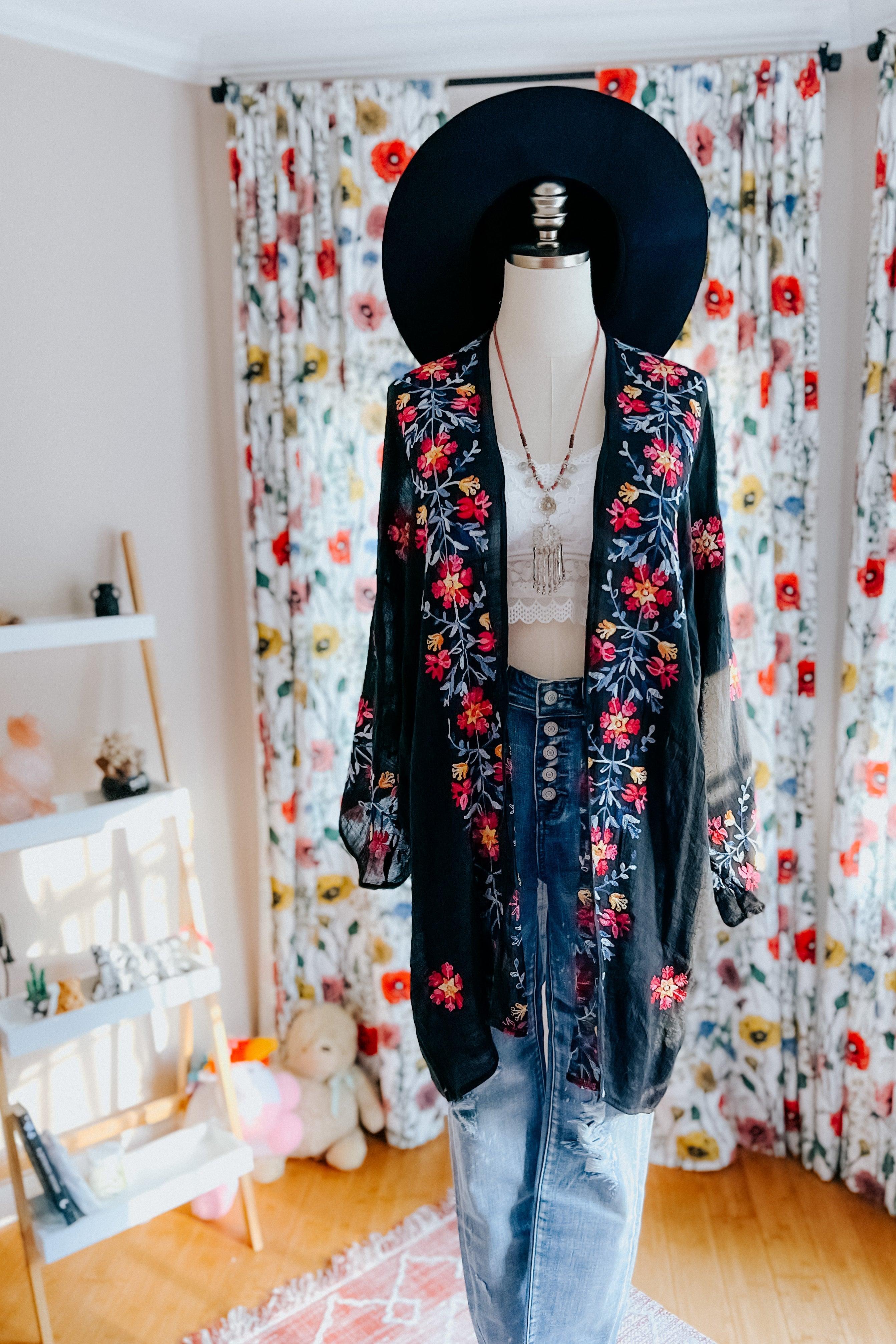 Mannequin dressed in black embroidered duster with floral pattern, layered over lace crop top and high-waisted jeans