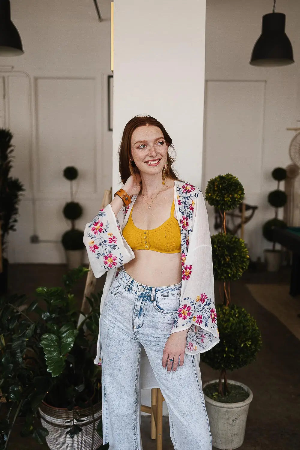 Woman wearing an ivory embroidered duster over a yellow top and high-waisted light wash jeans in indoor setting
