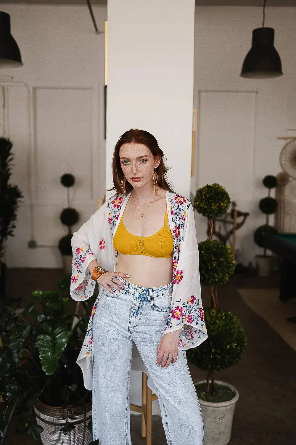 Woman wearing an ivory embroidered duster over a mustard yellow top and light-wash jeans in a stylish indoor setting