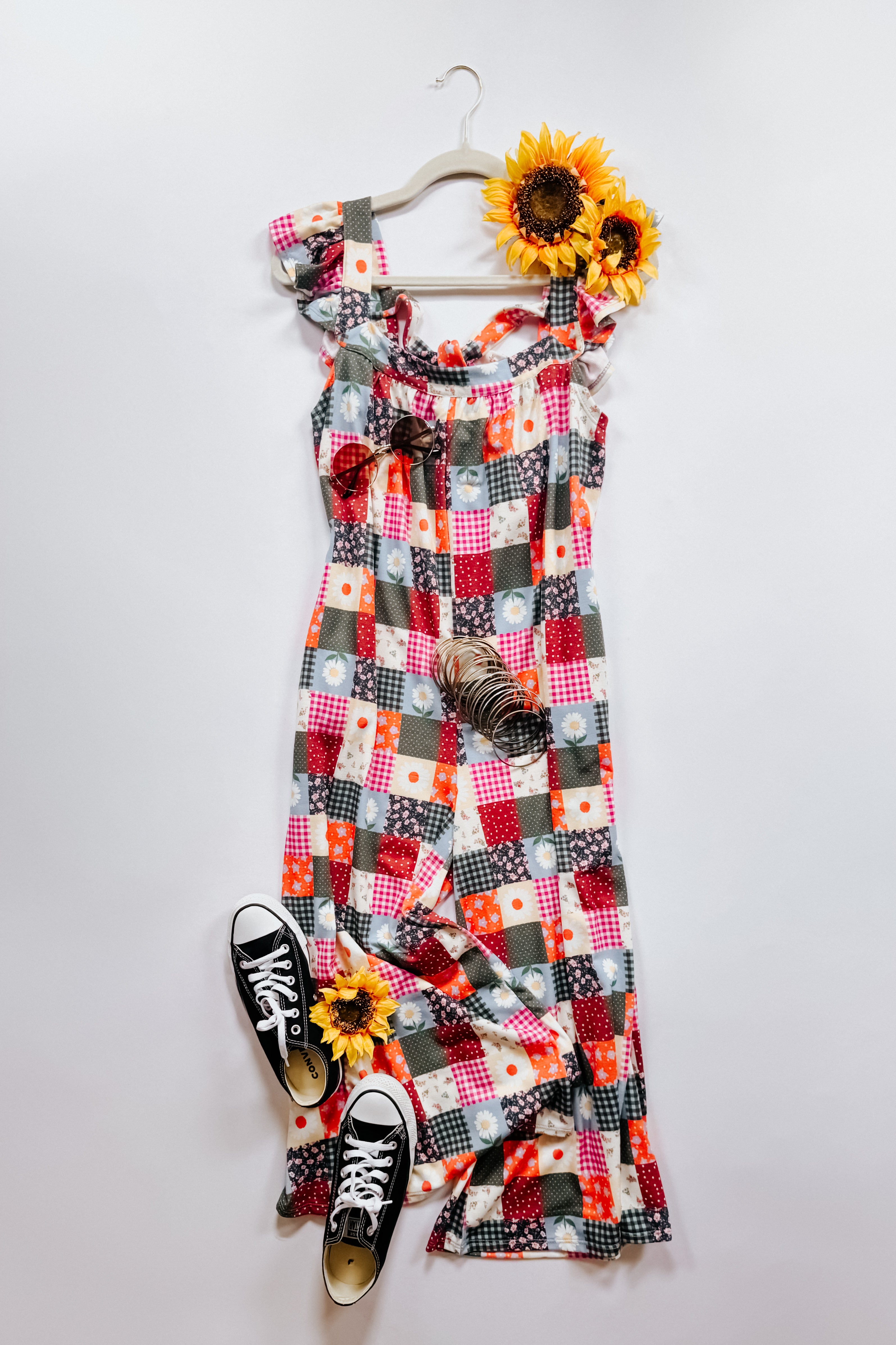 Multicolor patchwork jumpsuit with ruffle sleeves laid flat with black sneakers and sunflowers on white background