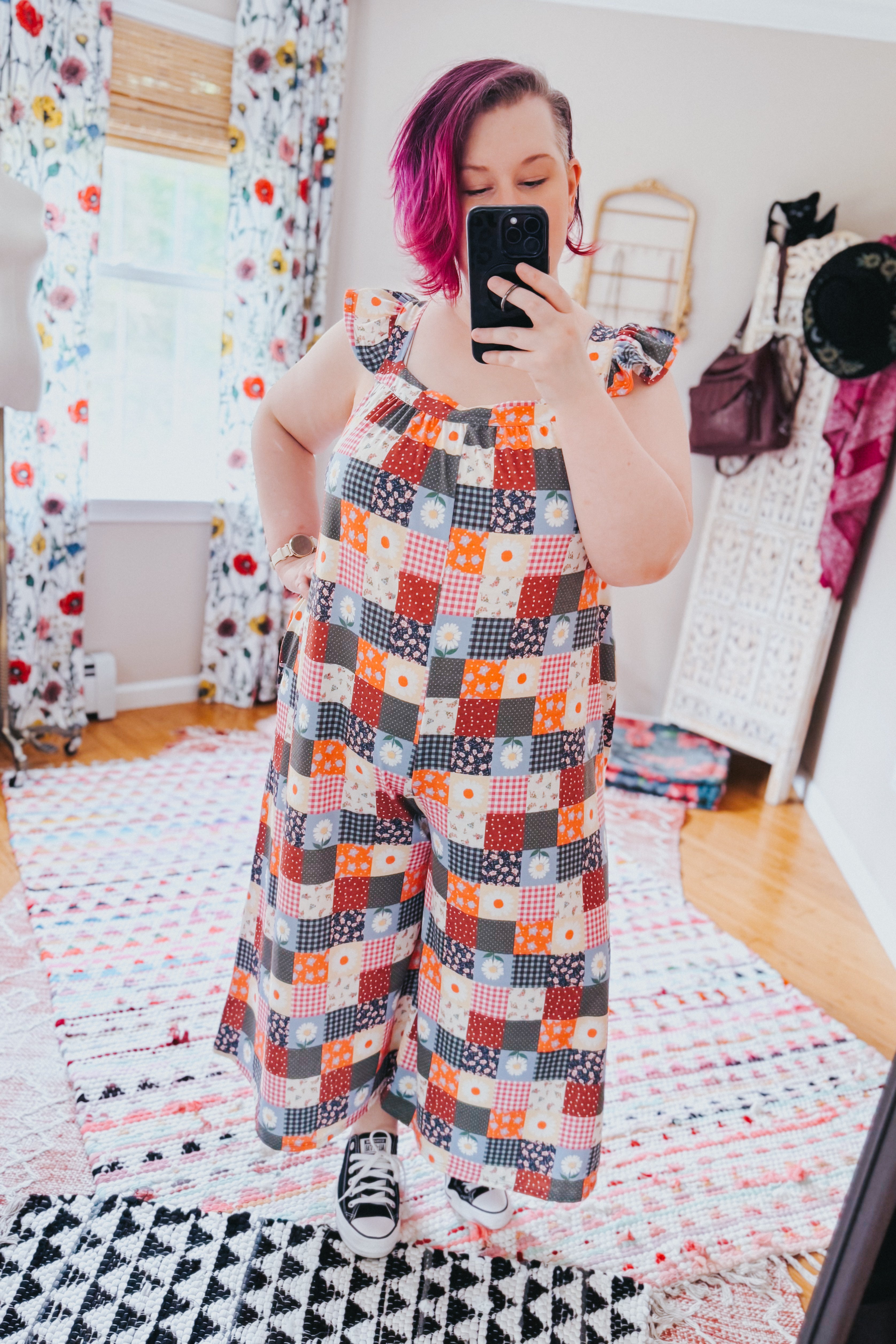 Woman with magenta hair wearing a multicolor patchwork jumpsuit with ruffle sleeves and wide legs in a bright room