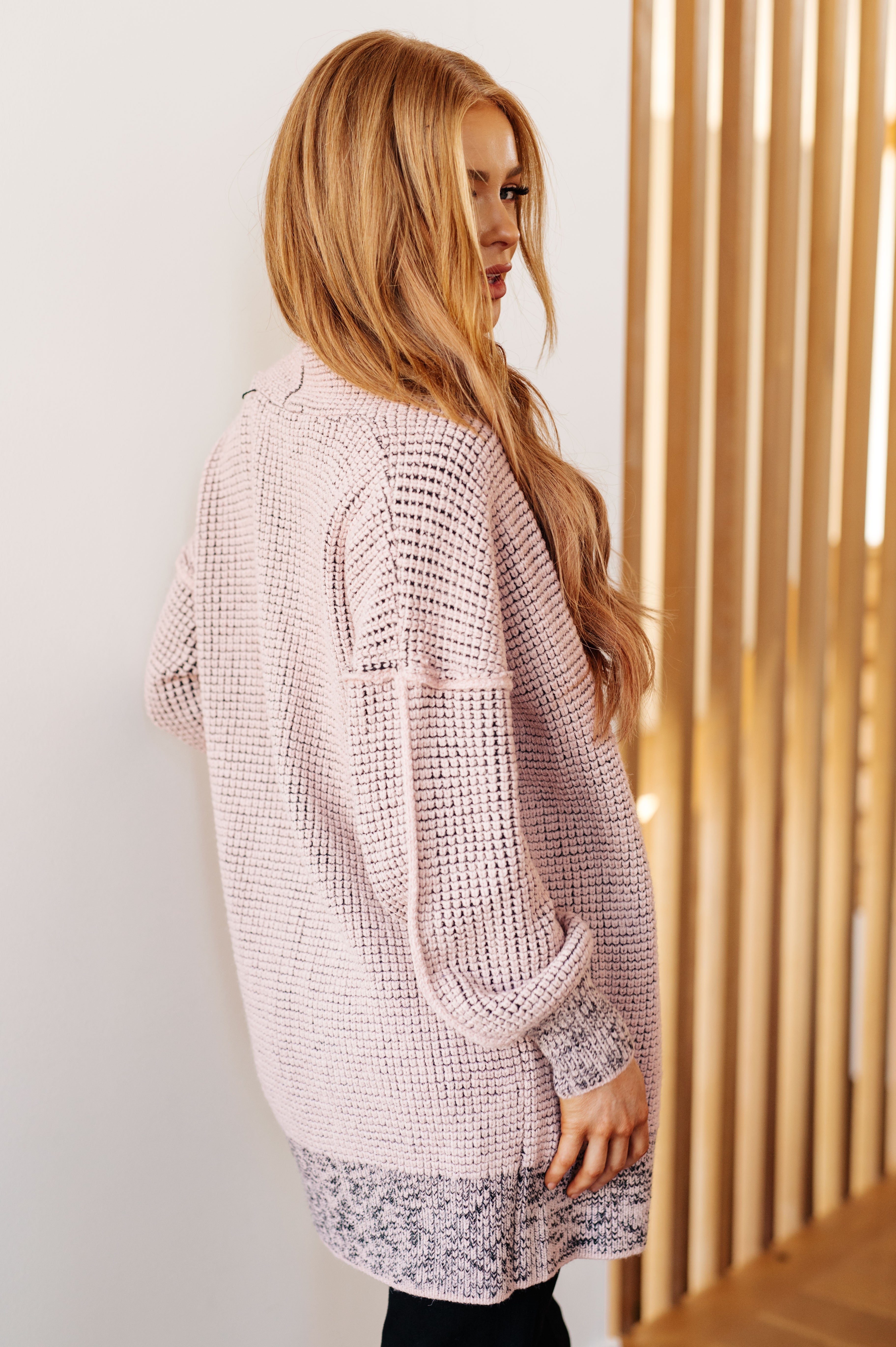 Side view of a woman wearing a plush mauve cardigan with textured knit and patterned hem in a warm indoor setting