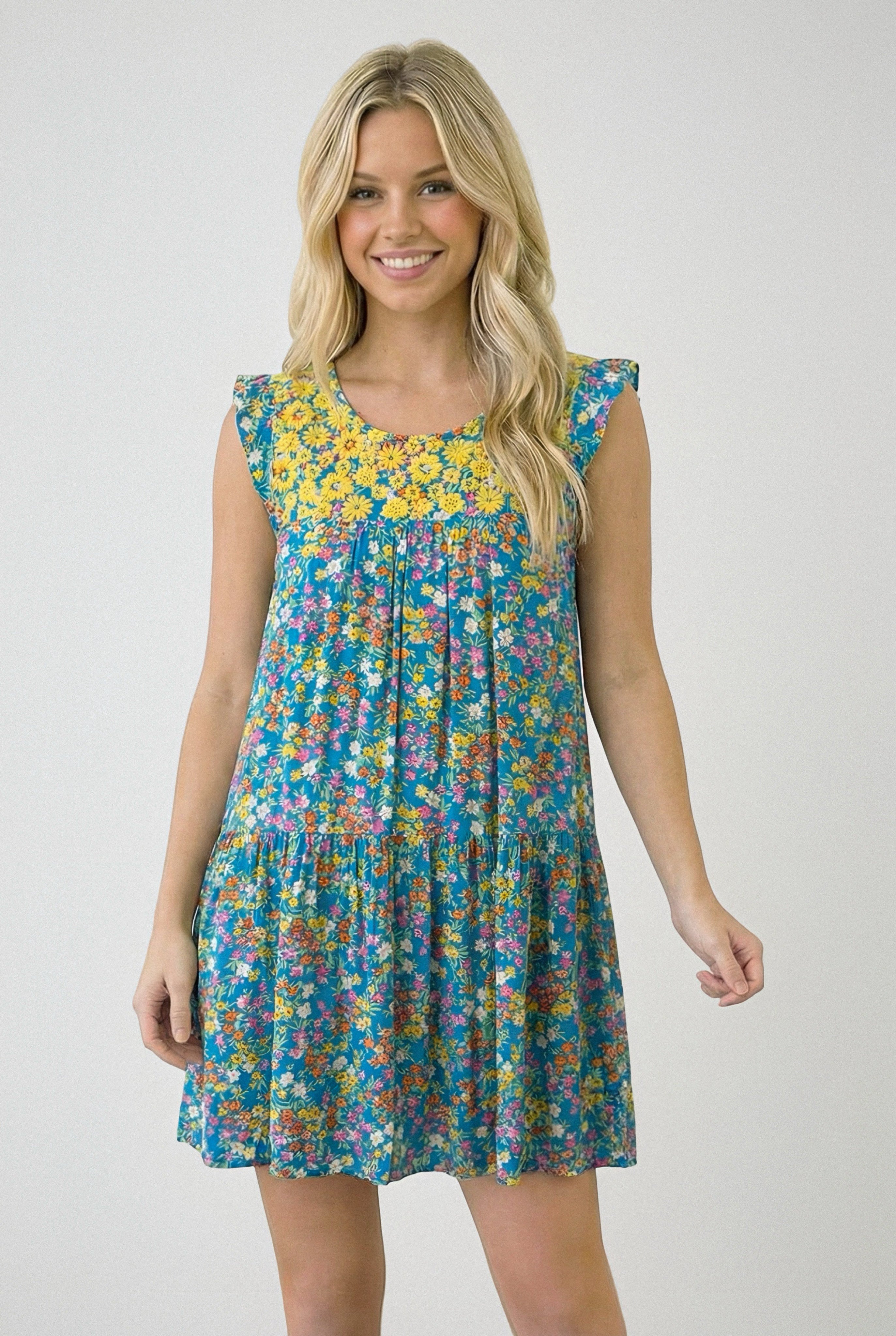 Woman wearing a sleeveless blue dress with yellow floral yoke and multicolored small flower print smiling