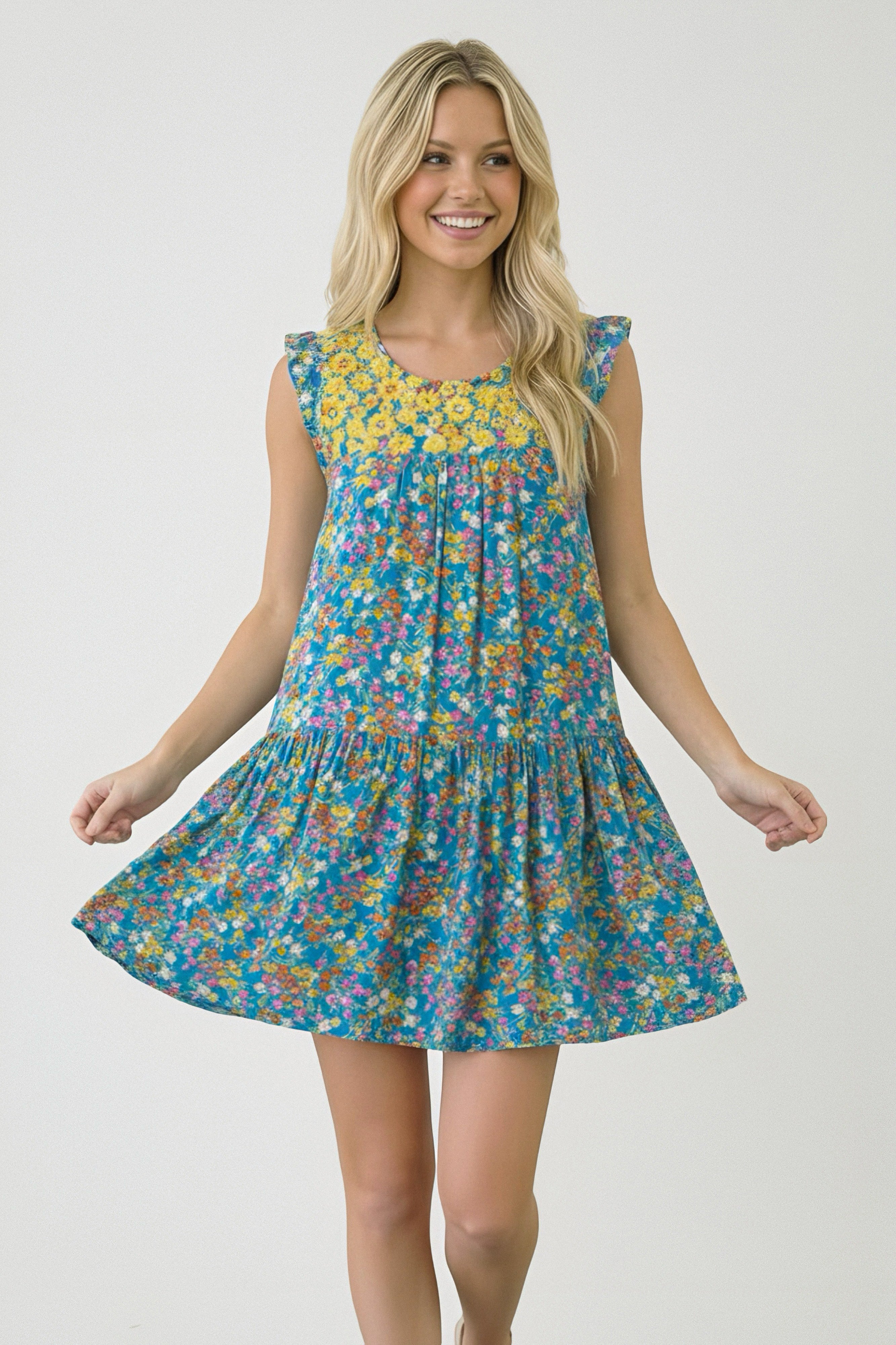 Smiling woman wearing a blue dress with yellow floral yoke and colorful all-over flower print twirling
