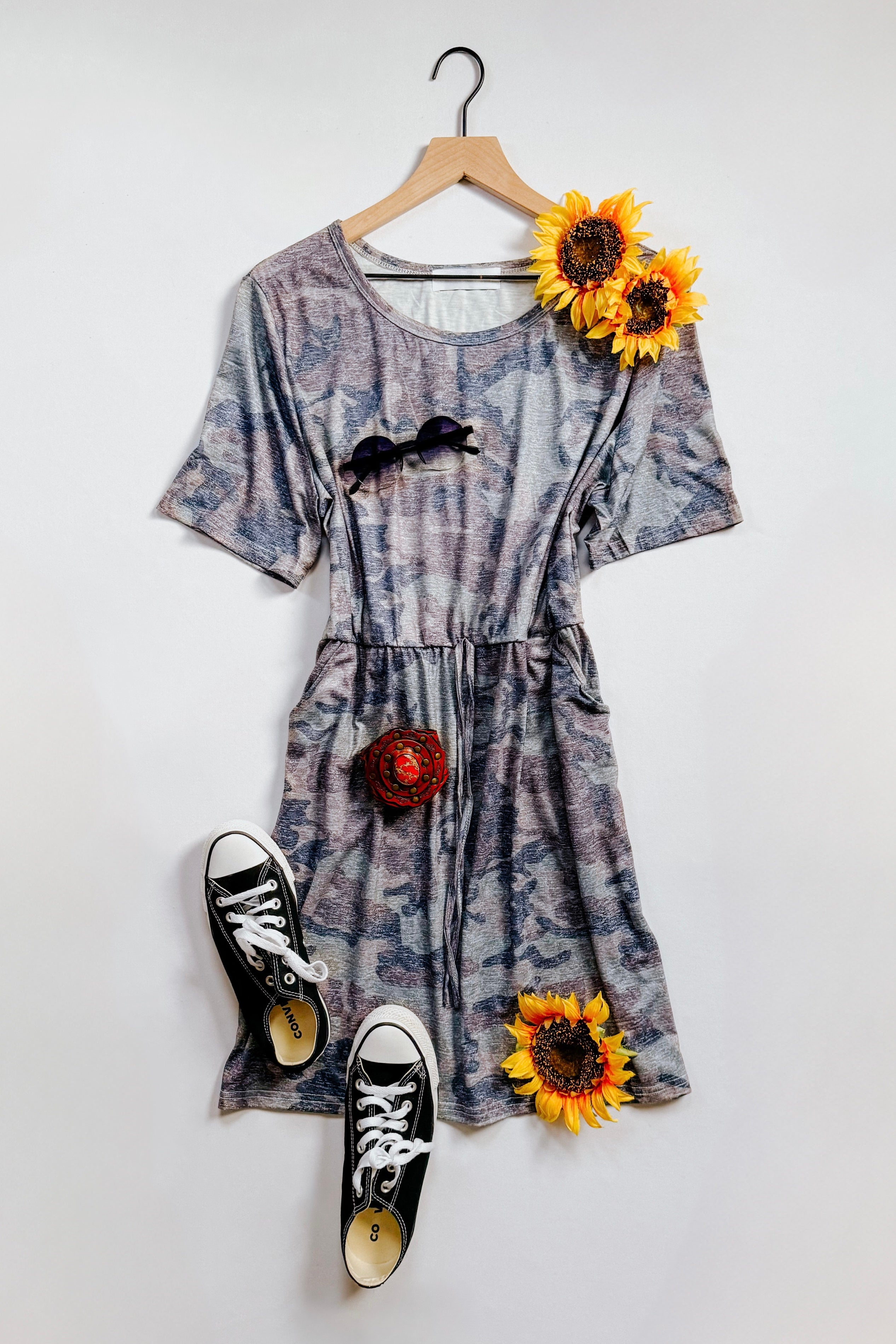 Blue vintage camo print dress with drawstring waist displayed with black sneakers and sunflowers on hanger
