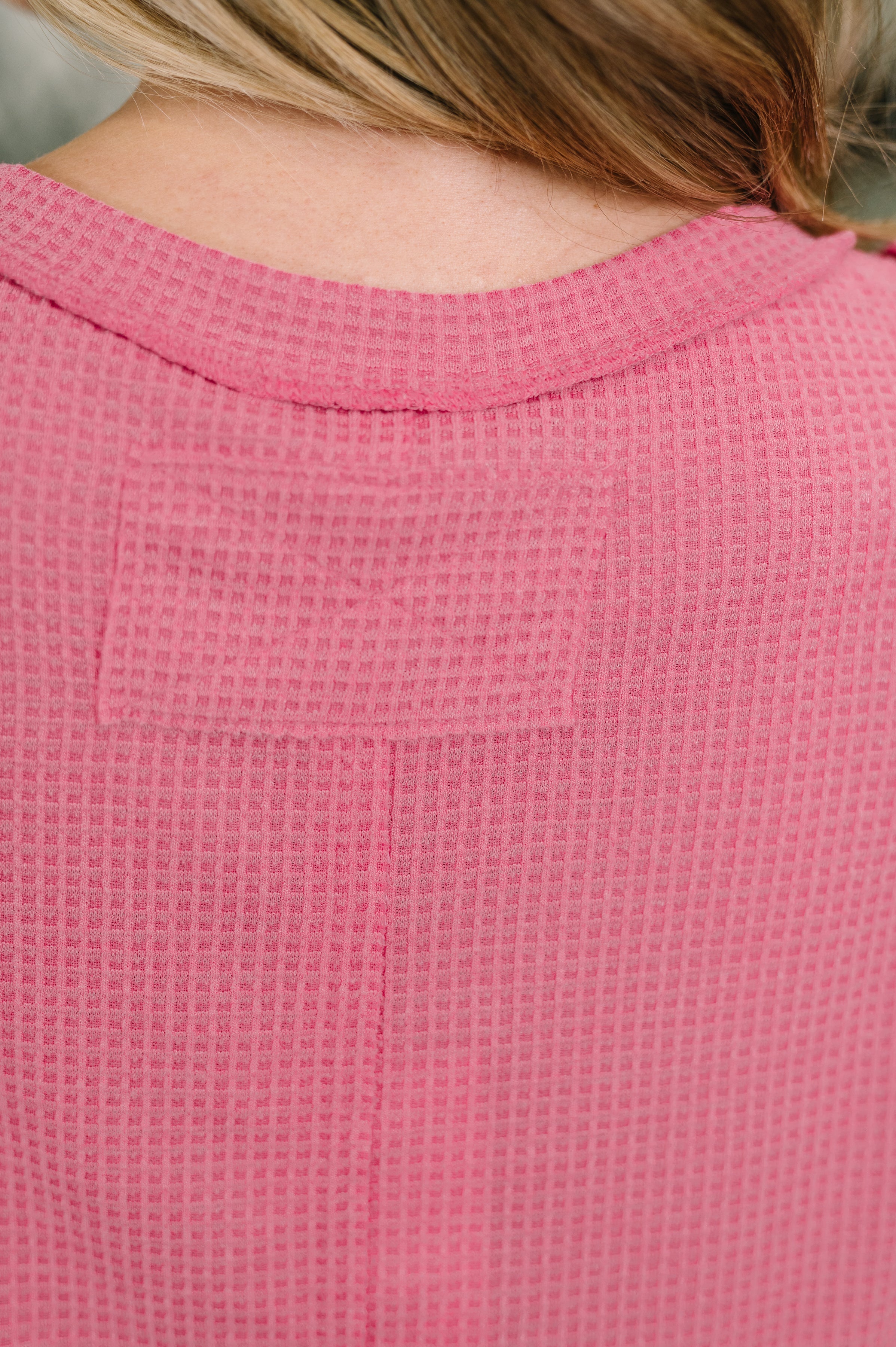 Close-up of pink waffle knit fabric with banded round neckline and exposed seam detail on upper back of tank top