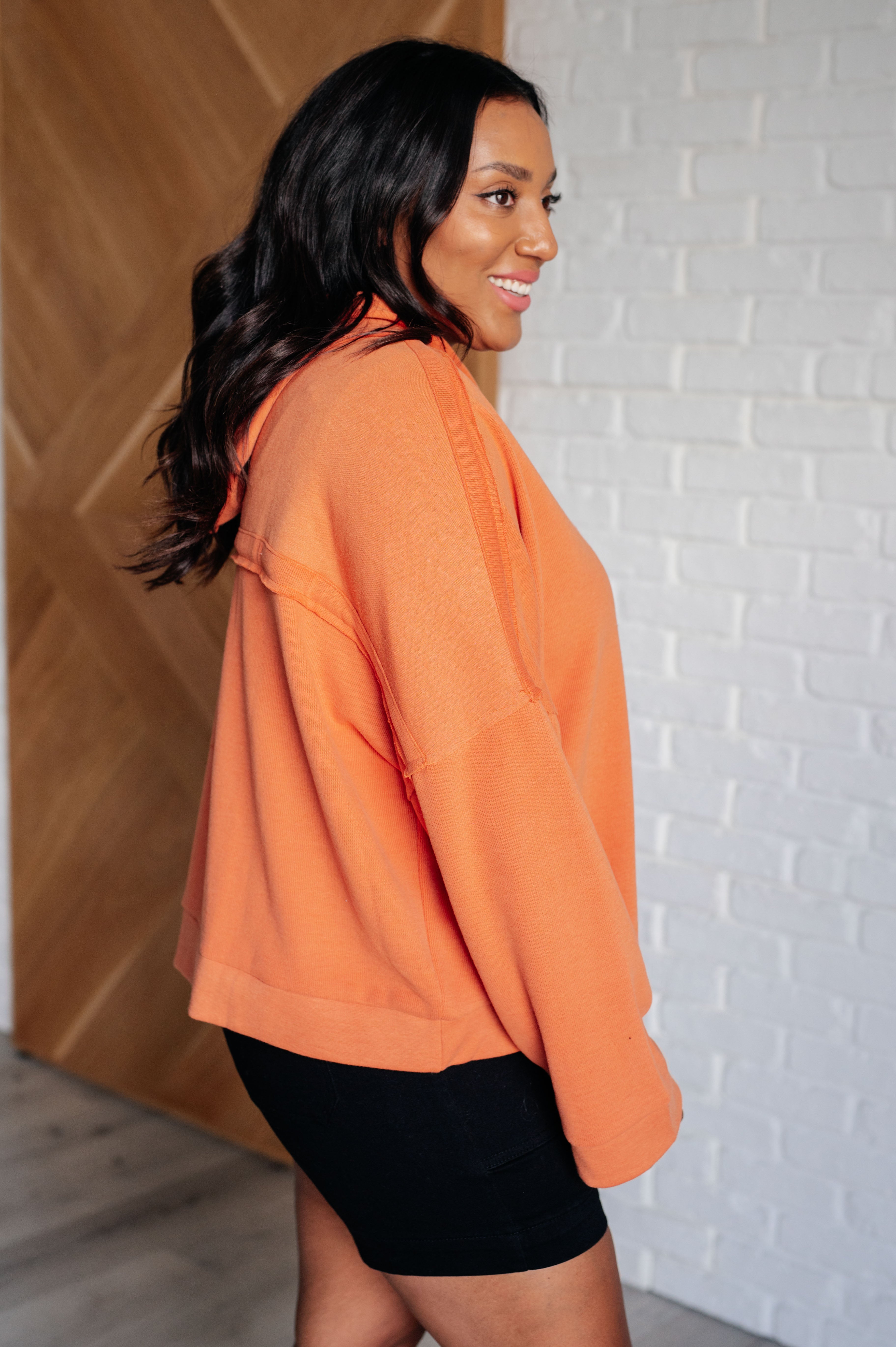 Woman wearing a vibrant orange relaxed-fit hoodie paired with black shorts standing indoors smiling confidently
