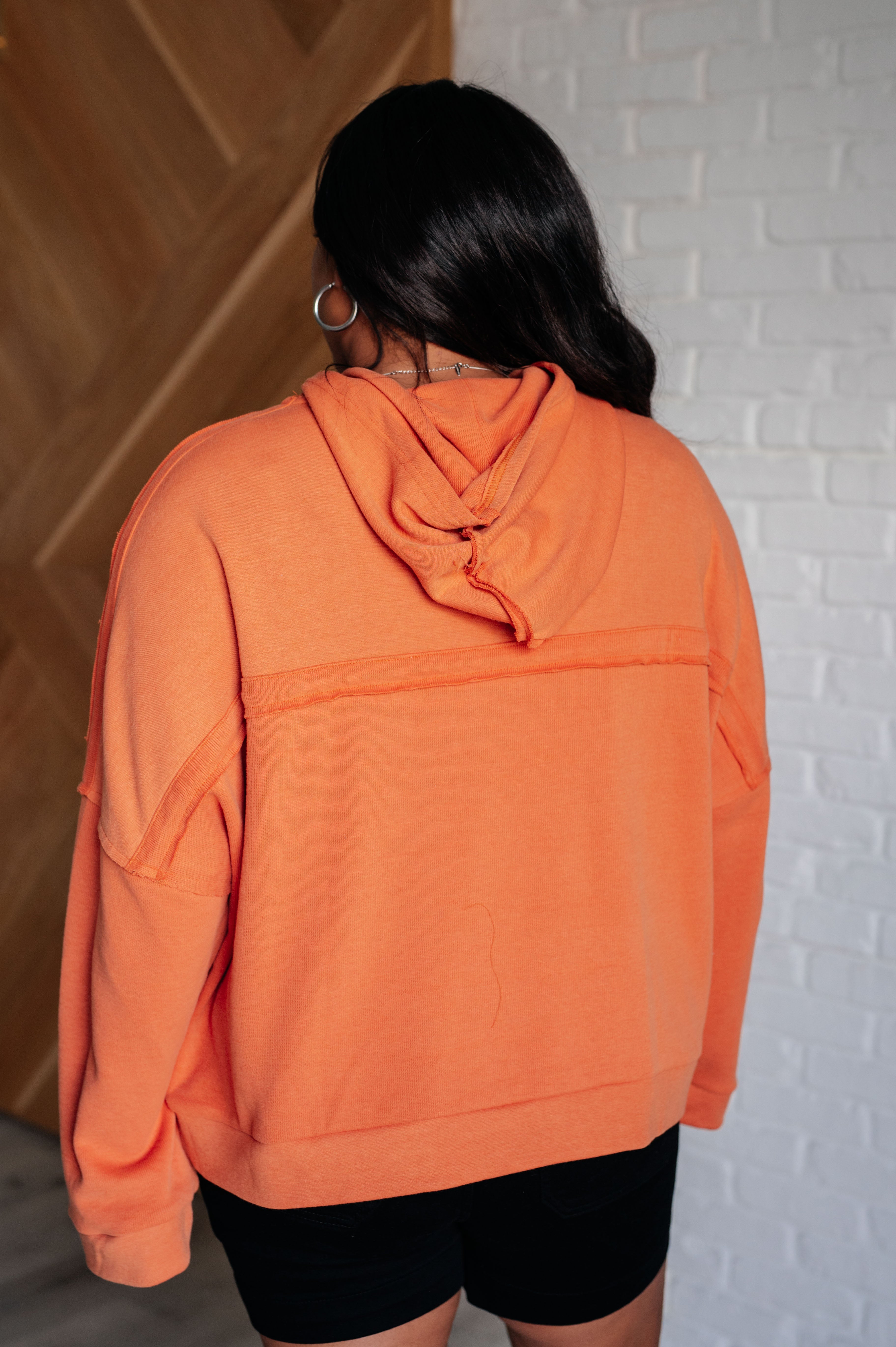 Woman wearing an oversized orange hoodie with dropped shoulders and visible seam details in a cozy indoor setting