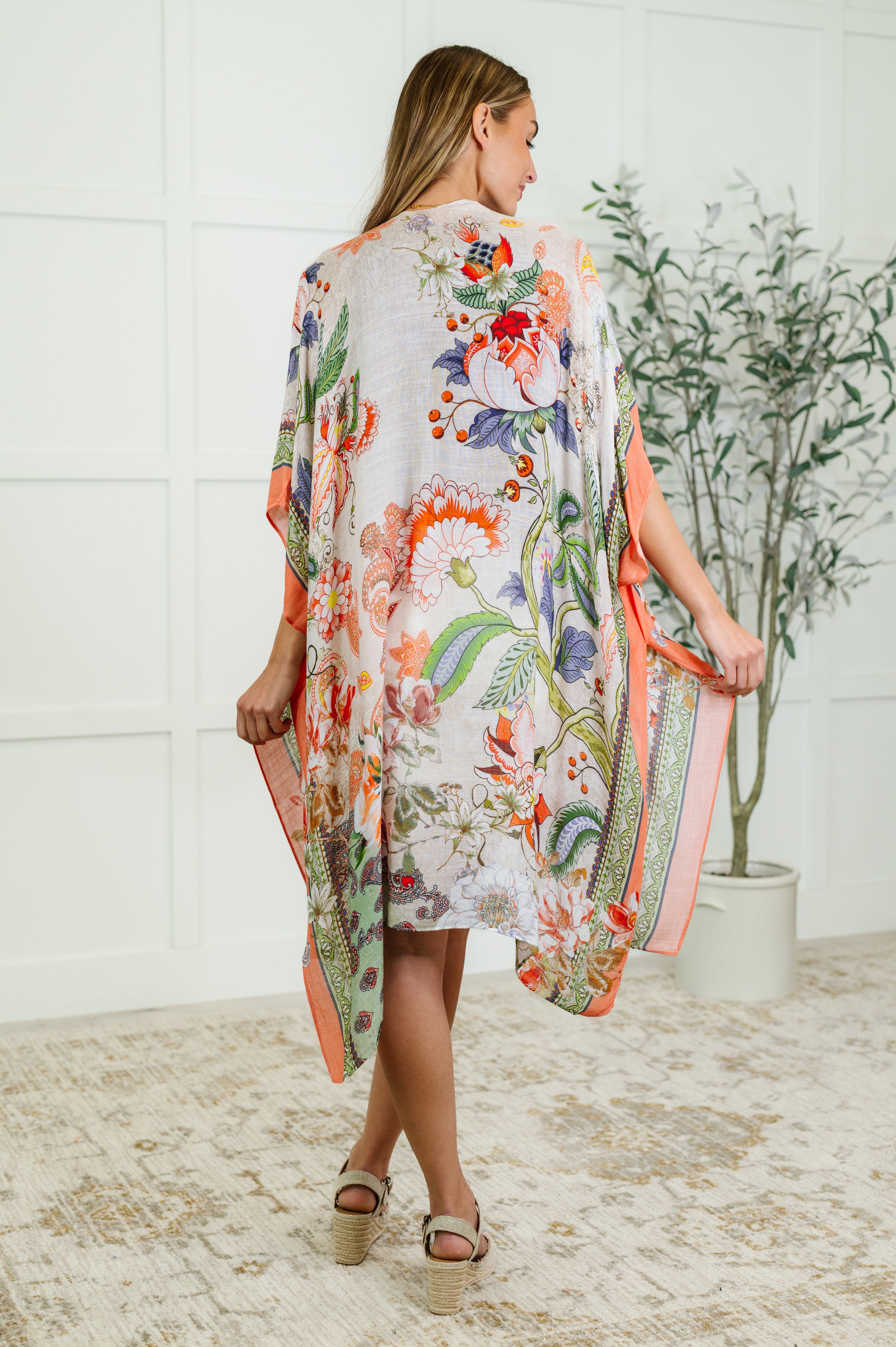 Rear view of woman wearing a lightweight orange and green floral patterned kimono standing indoors near a plant