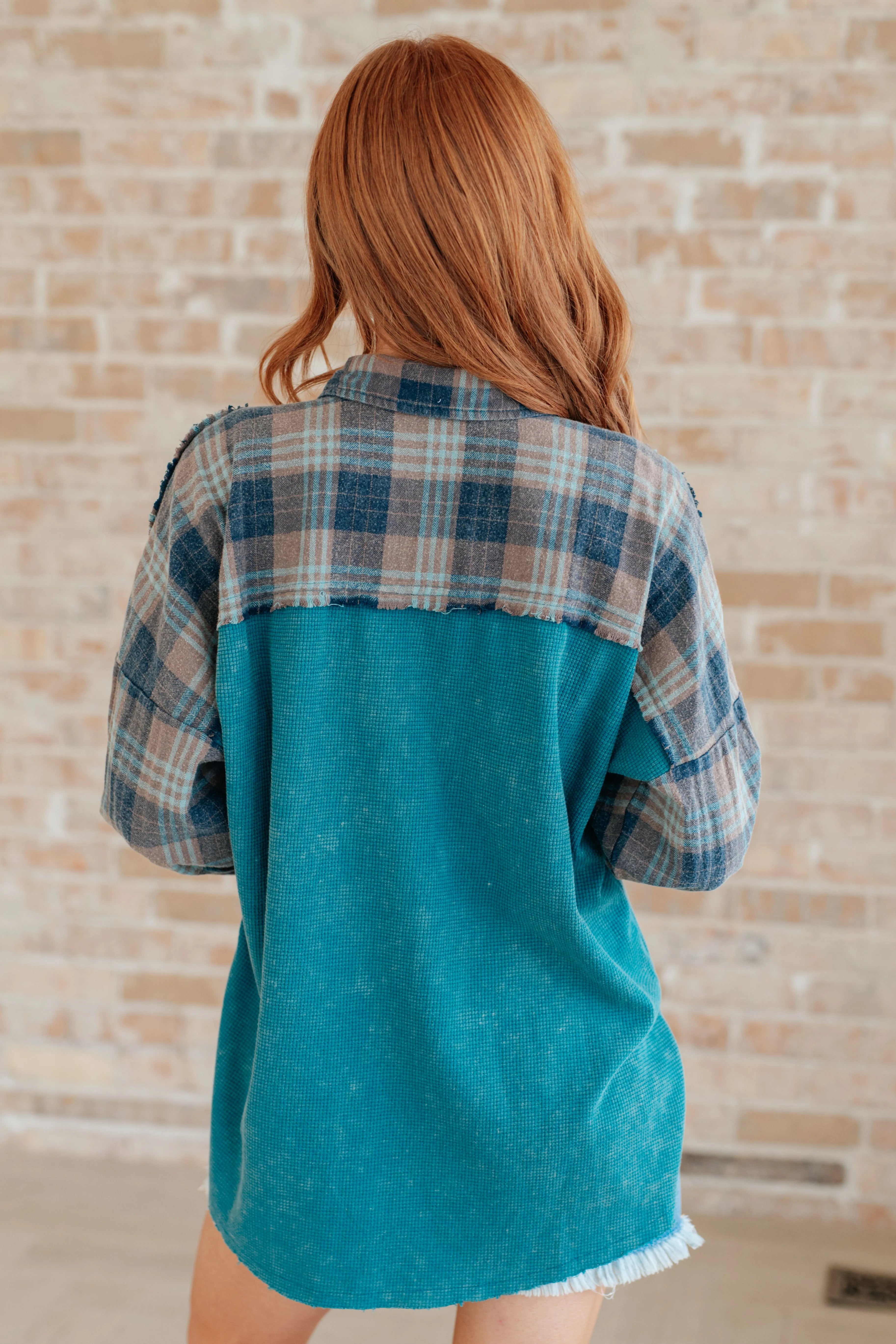 Woman wearing a teal thermal plaid button-up with a relaxed fit and frayed hem standing indoors with back visible