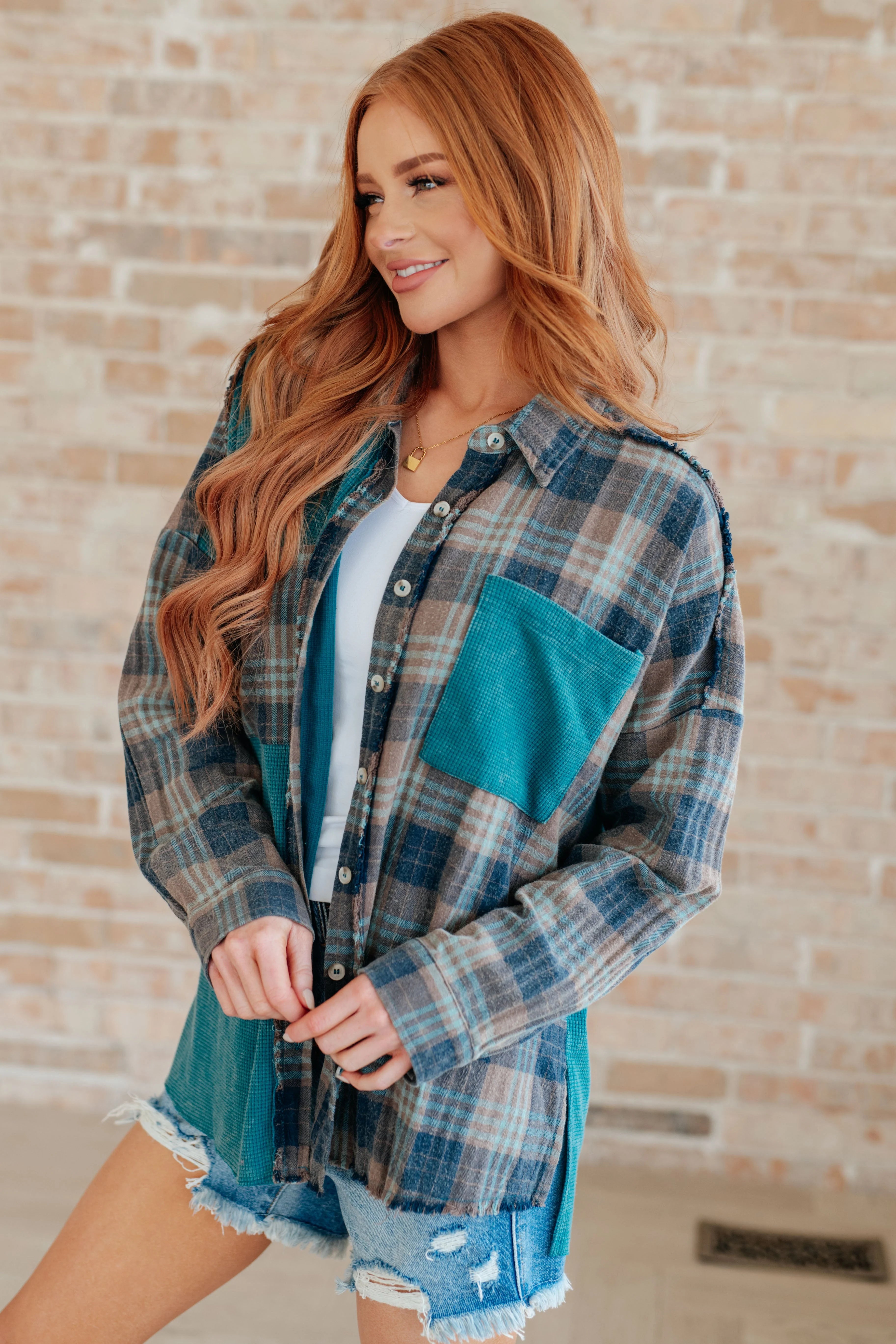 Woman wearing teal and gray plaid thermal button-up with textured pocket and distressed denim shorts indoors