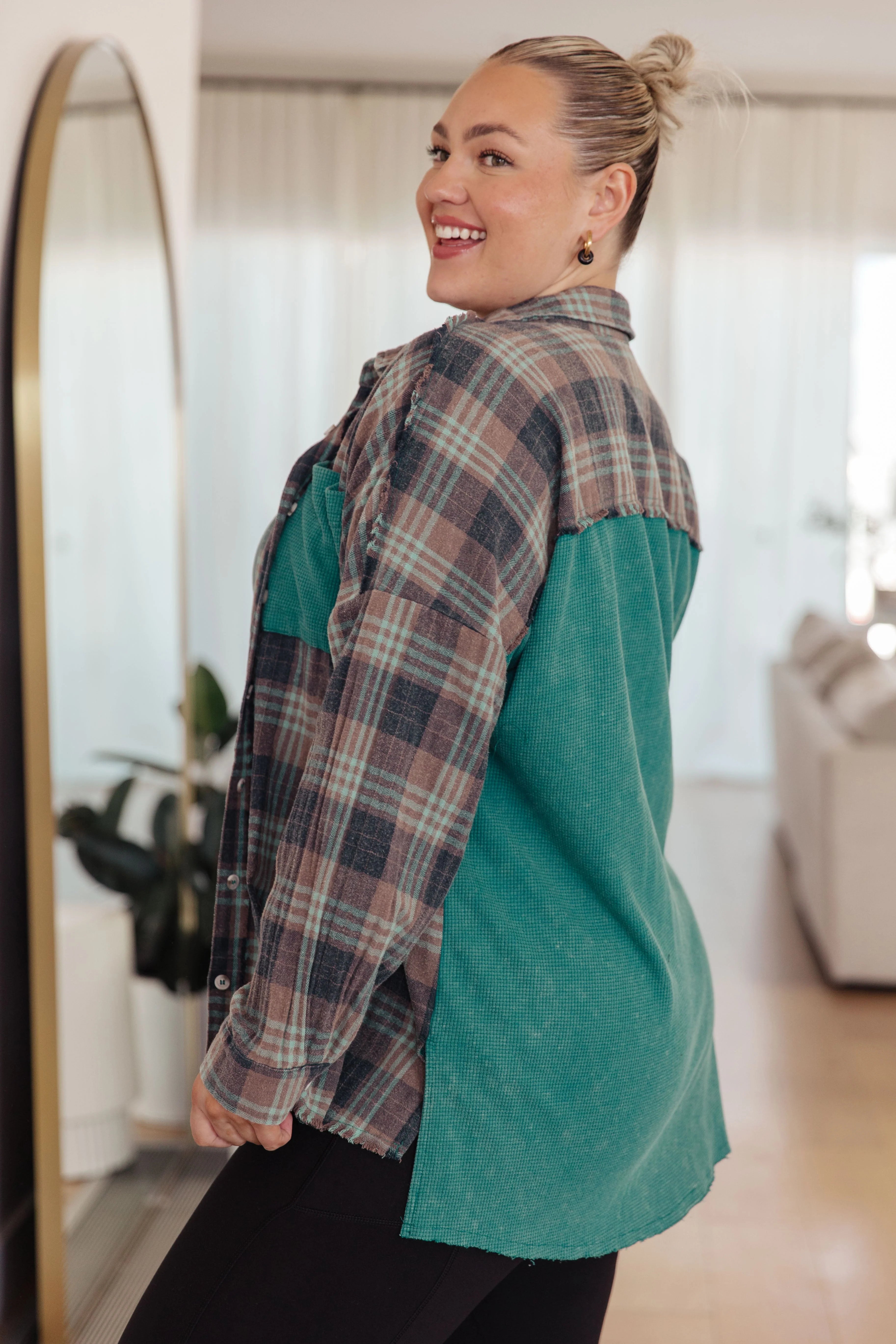 Smiling woman wearing a teal and plaid thermal button-up shirt indoors with hair in a bun and gold earrings