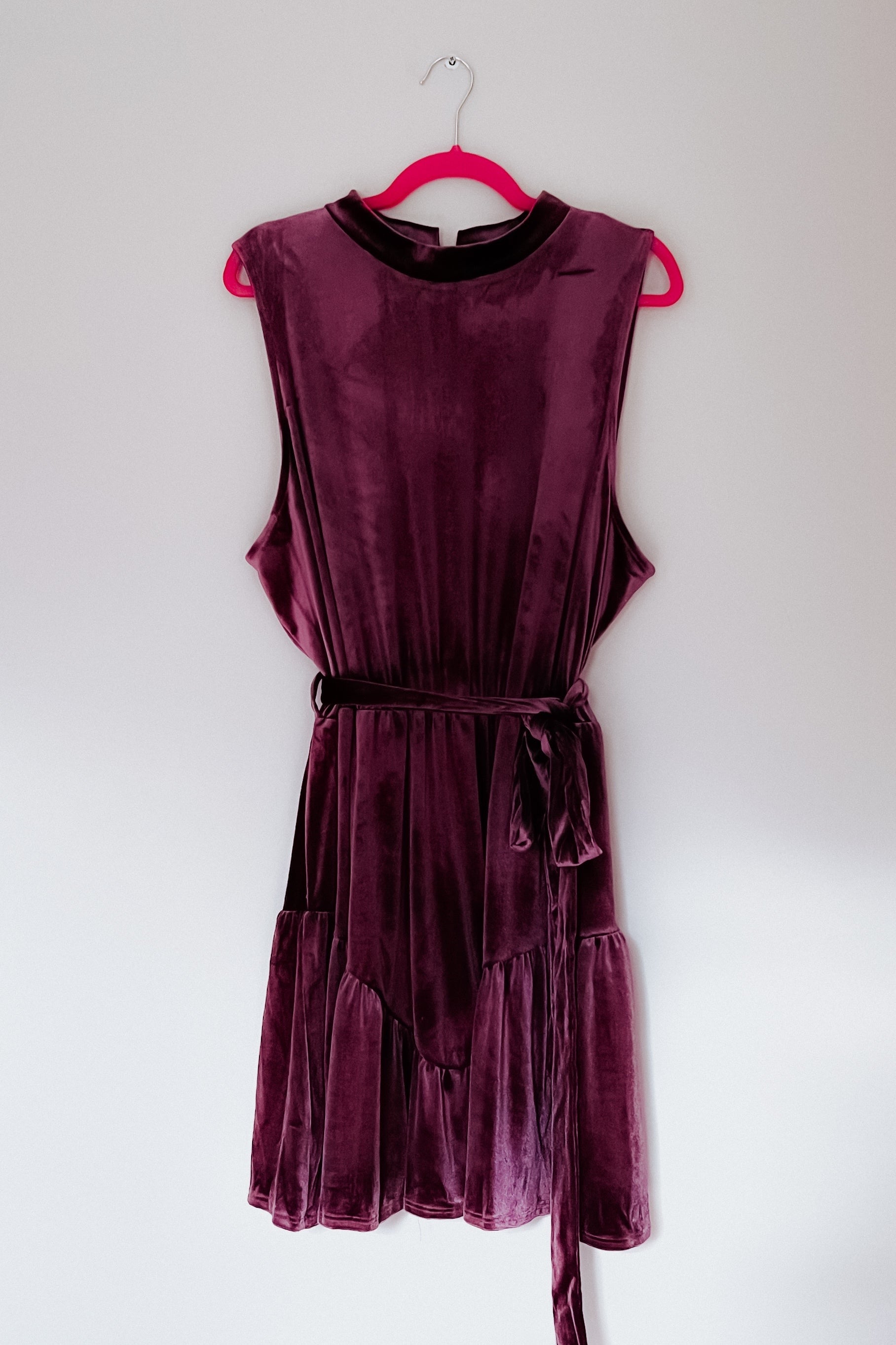 Sleeveless purple velvet dress with a tied waist bow, soft texture, and a relaxed fit hanging on a pink hanger